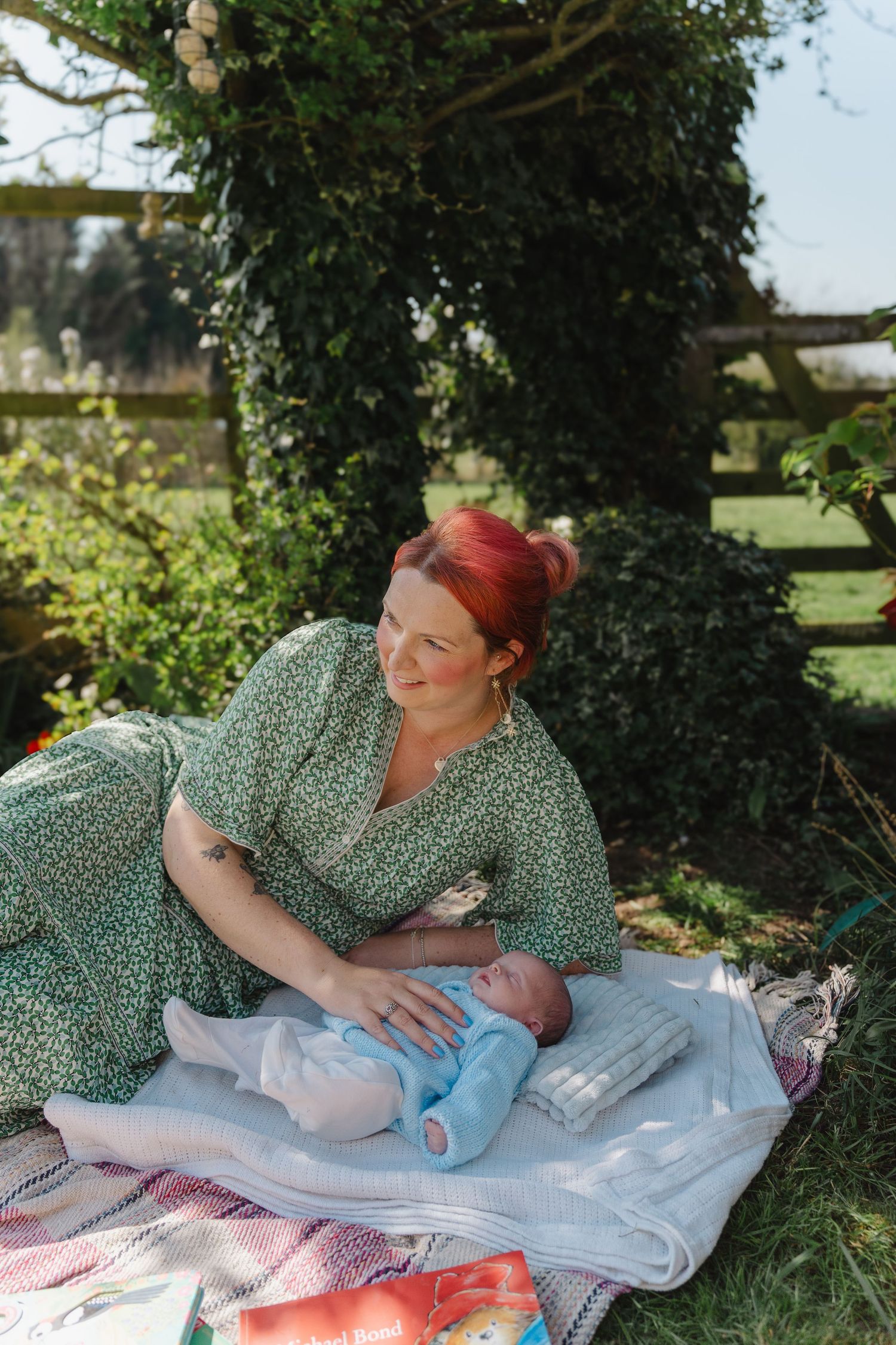 A picnic scene in a garden with a floral dress and blanket laid out on green grass under leafy trees.