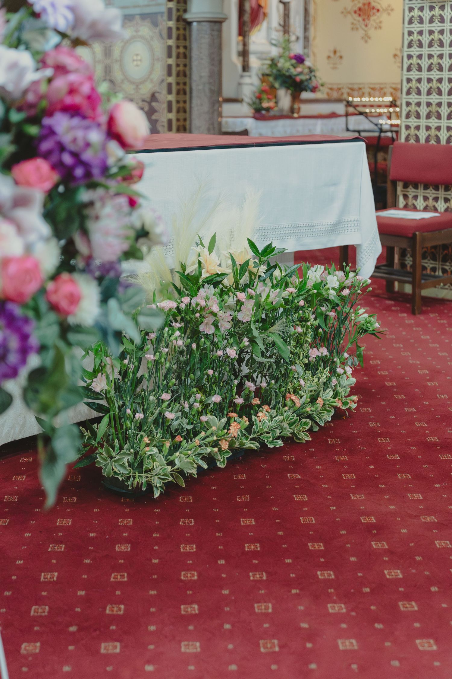 Decorative green floral arrangements on a red patterned carpet in an elegant interior setting.