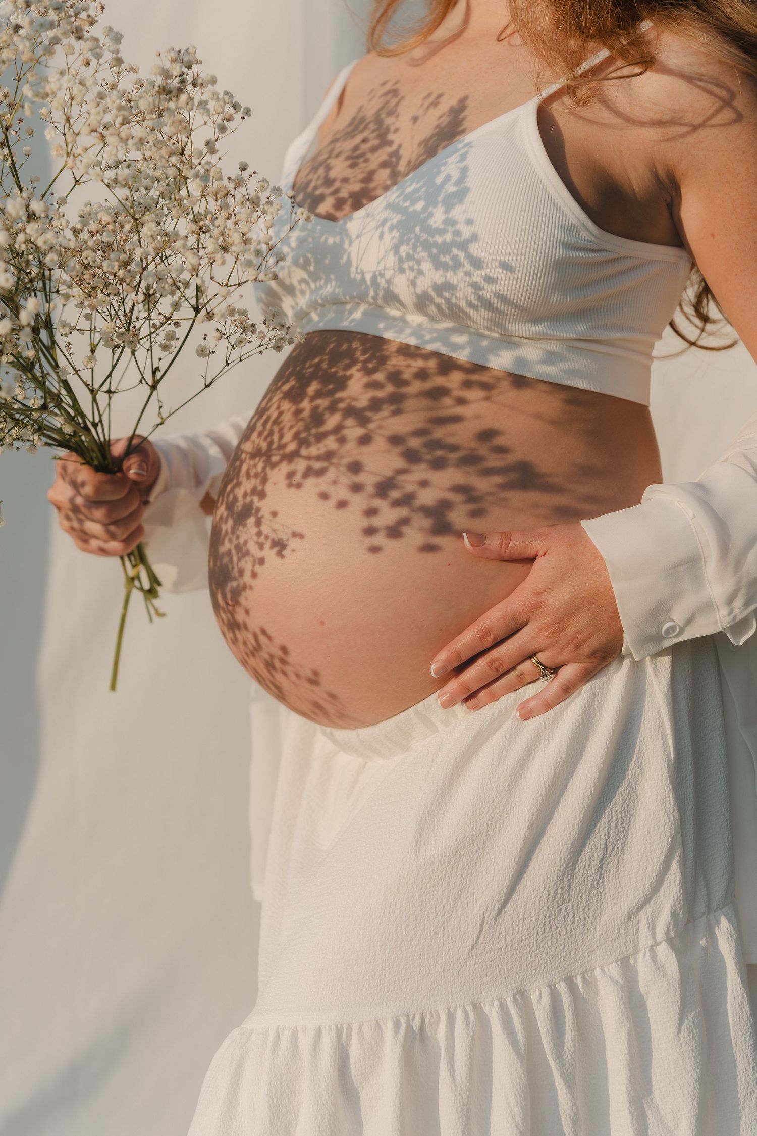 Sunlit maternity photos showing baby bump with delicate lace shadows.