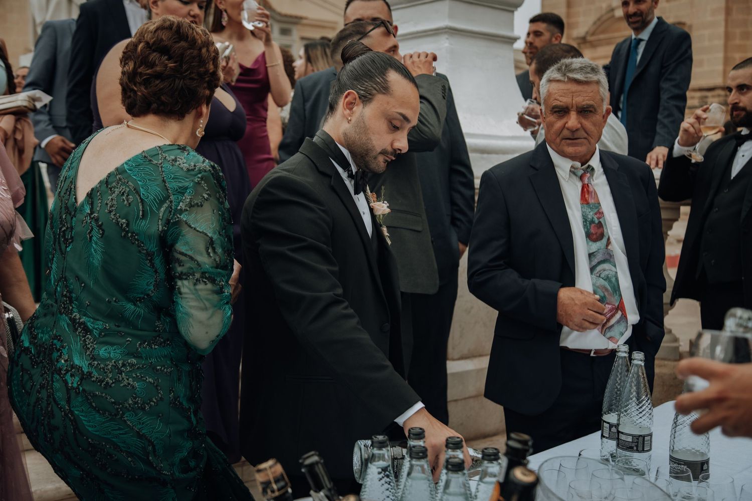 Wedding guests gather around a drink station during an outdoor reception celebration.