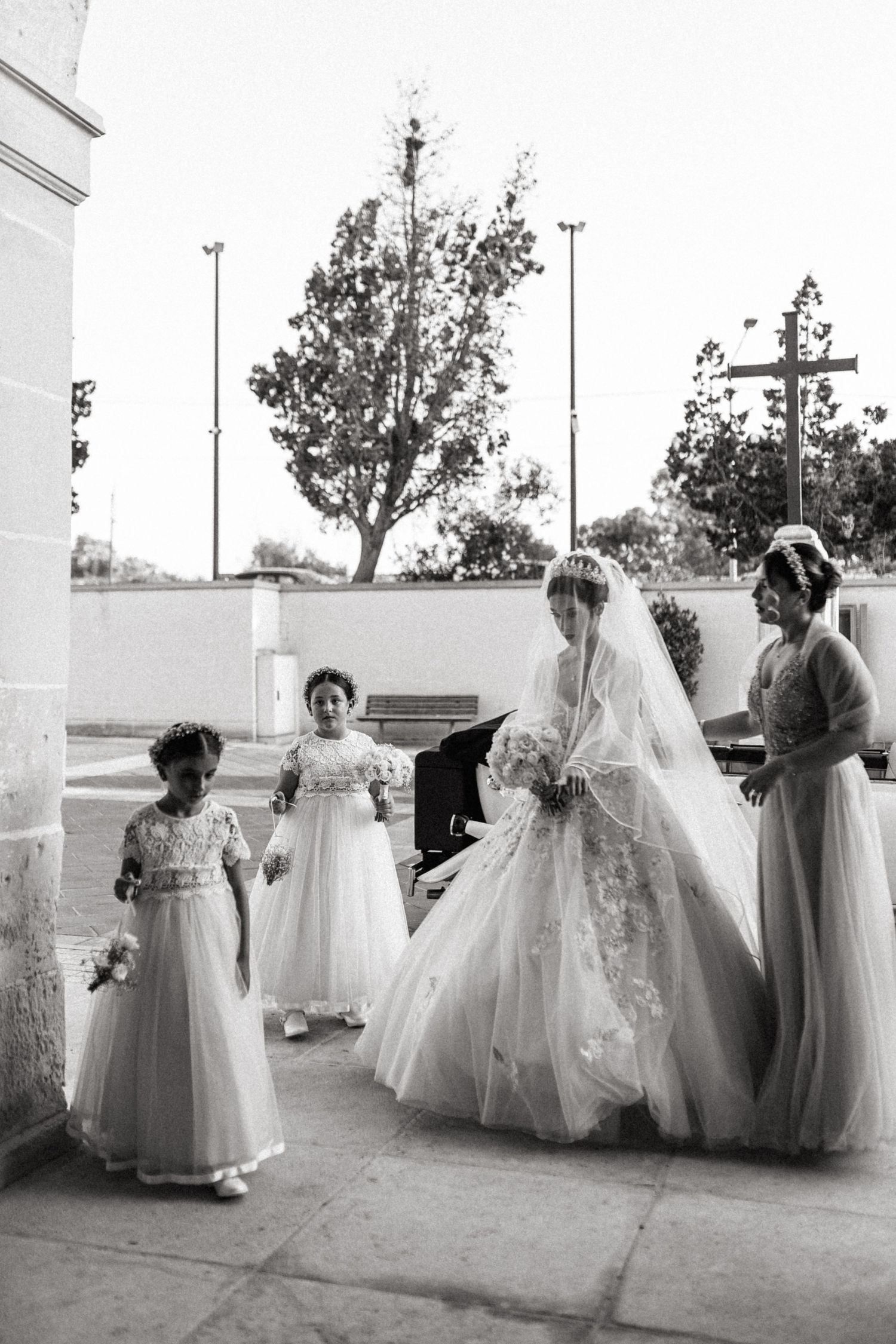 Black and white photo of bridal party with flower girls outside church entrance.