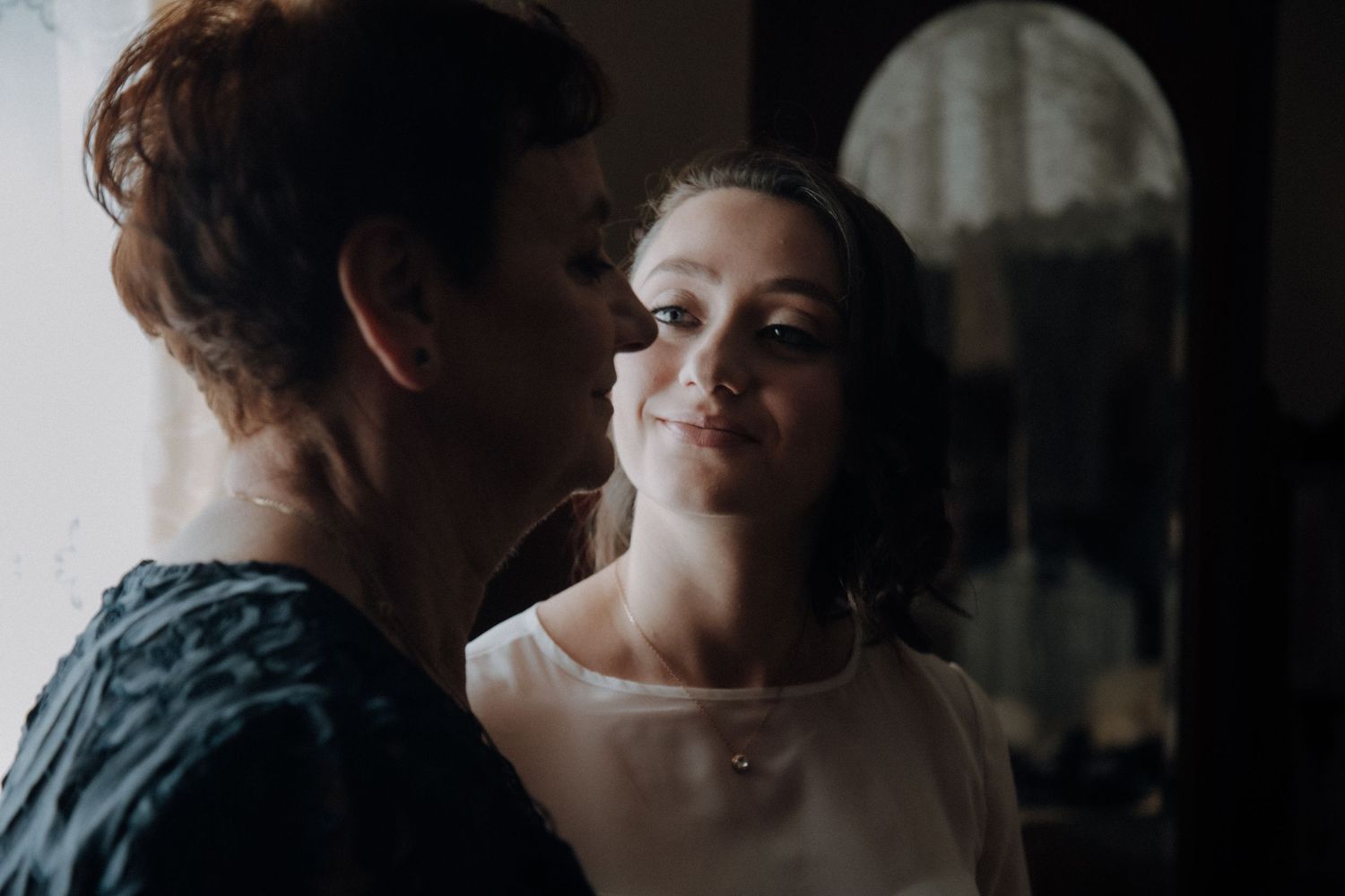 Two people share an intimate moment in moody lighting during wedding preparations.