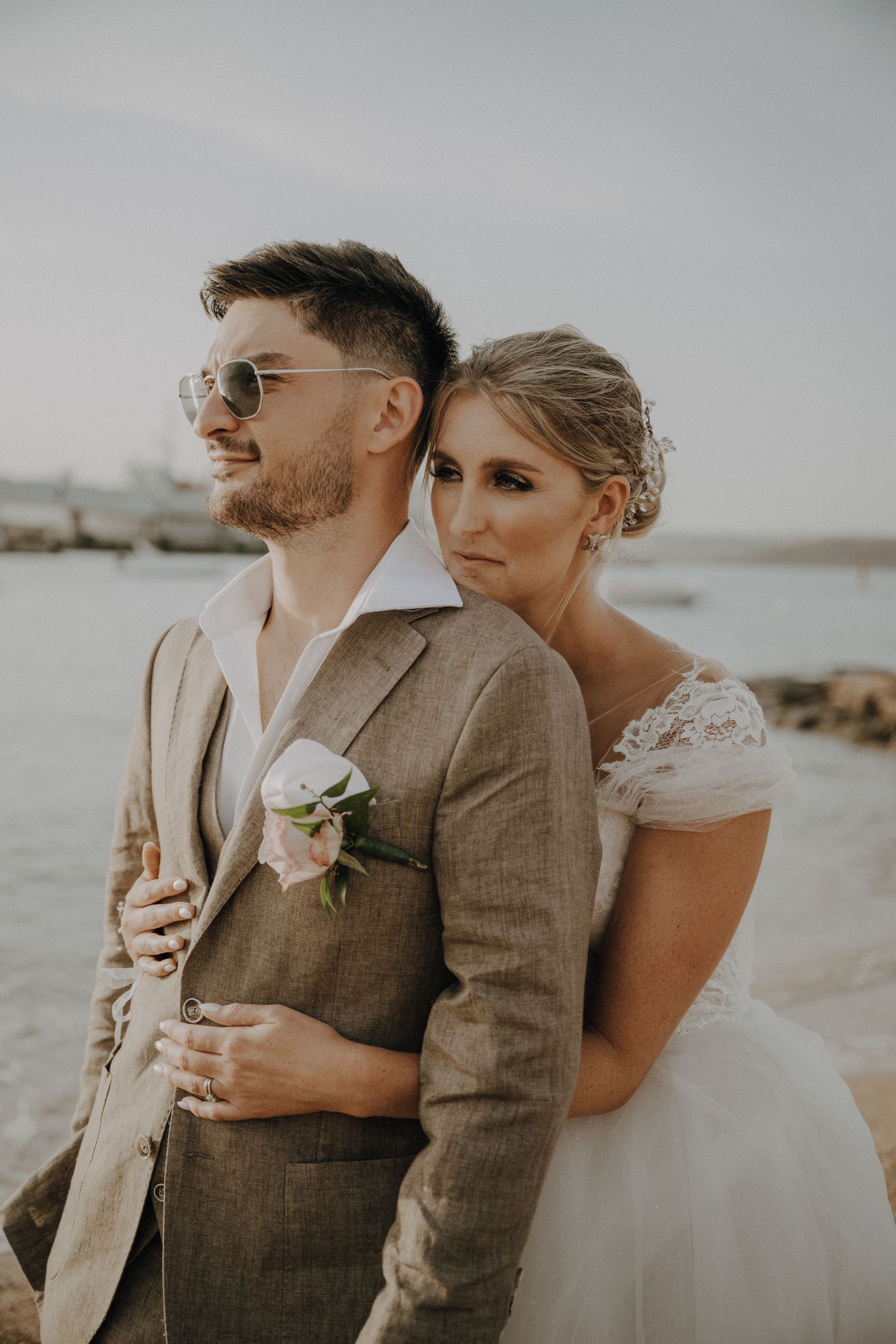 A romantic wedding photo of newlyweds embracing on a coastal beach in formal attire.