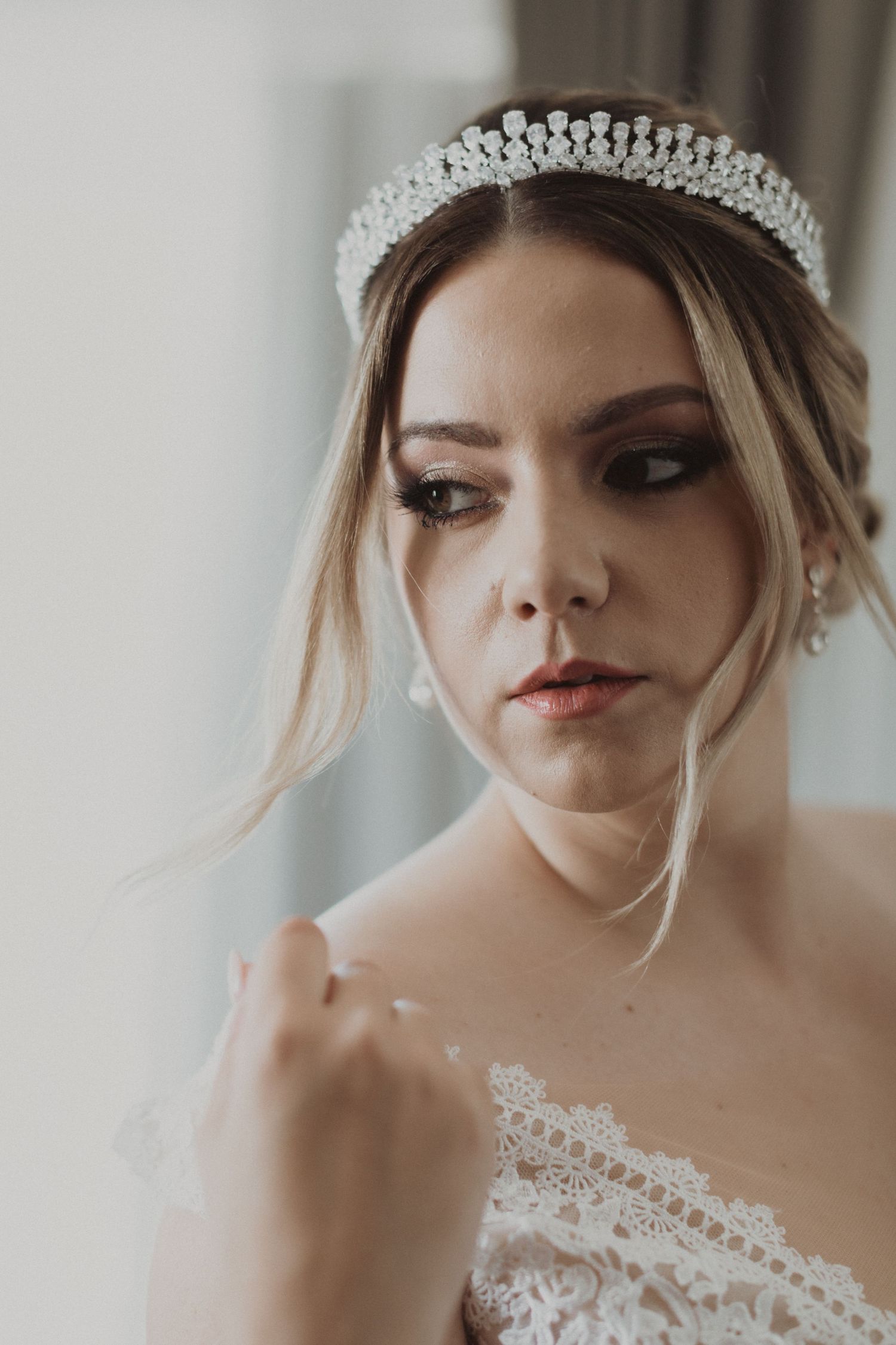 Close up portrait of a bride wearing a delicate crystal tiara and lace dress with dramatic eye makeup.