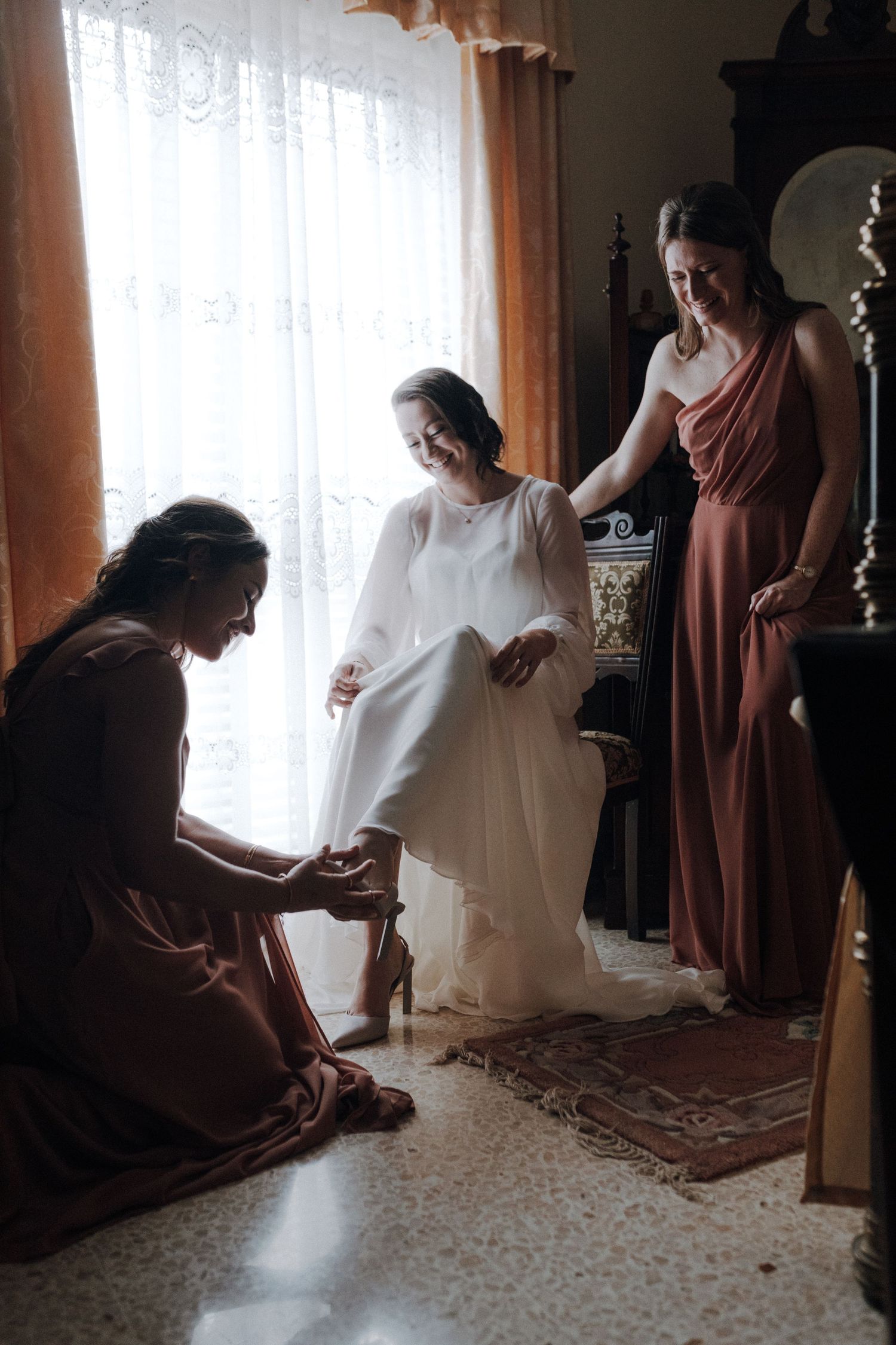 Wedding party getting ready in a room with natural window light and burgundy bridesmaid dresses.