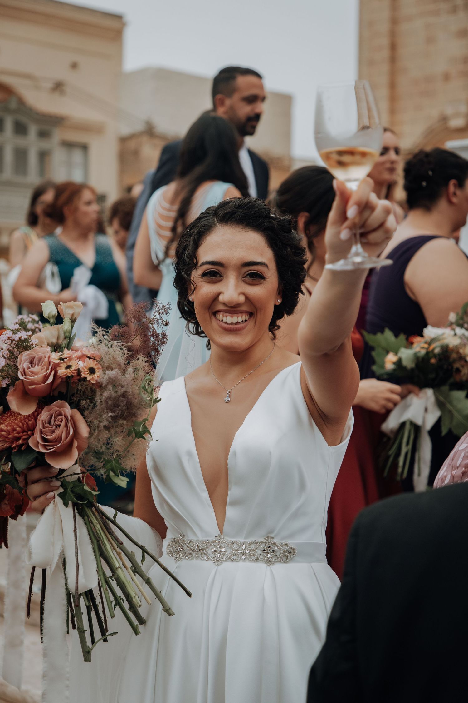 A joyful bride raises her wine glass in celebration while holding a romantic bouquet of roses.