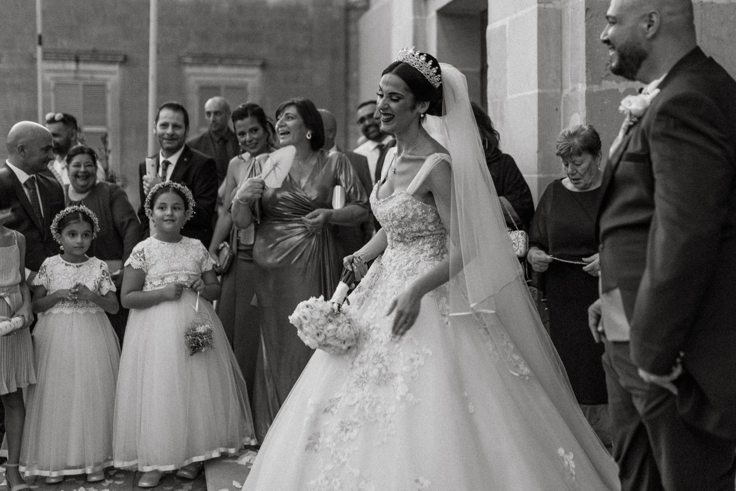 A joyful wedding party poses together after the ceremony in black and white photography.