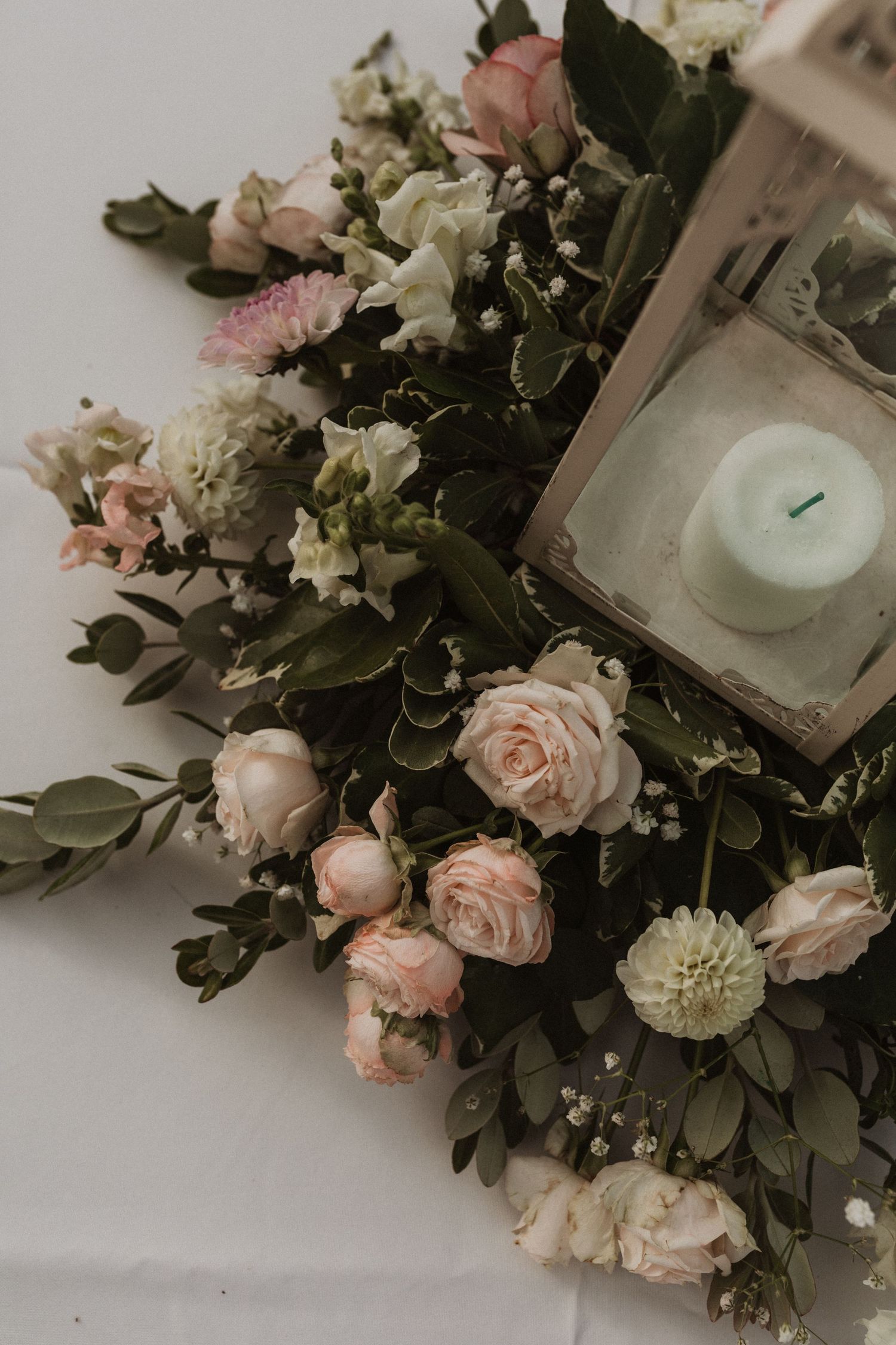 Romantic floral arrangement featuring blush roses and greenery on white surface.