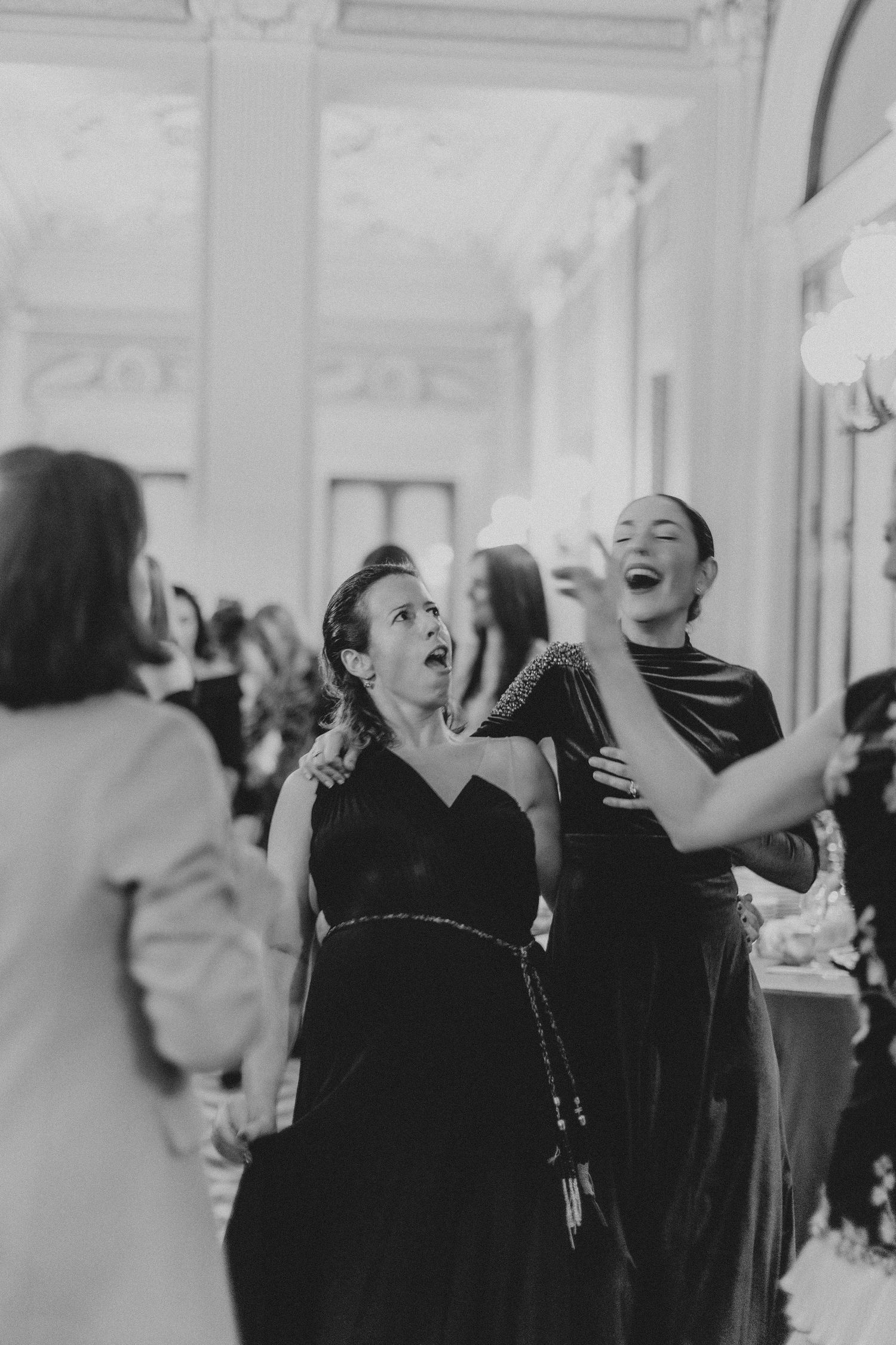 Two women sharing a candid moment of laughter at an elegant indoor event.