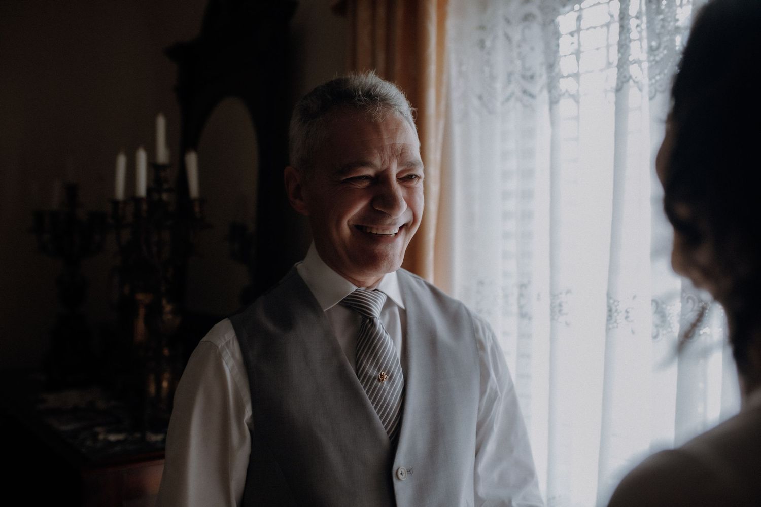 A warm smile lights up the face of someone wearing a light grey vest and tie.