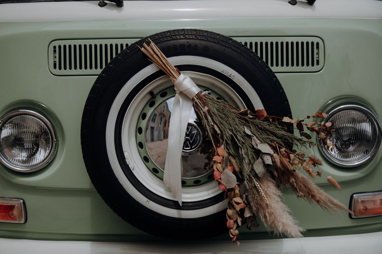 Close-up of vintage car's front grille and headlights with decorative dried flowers.