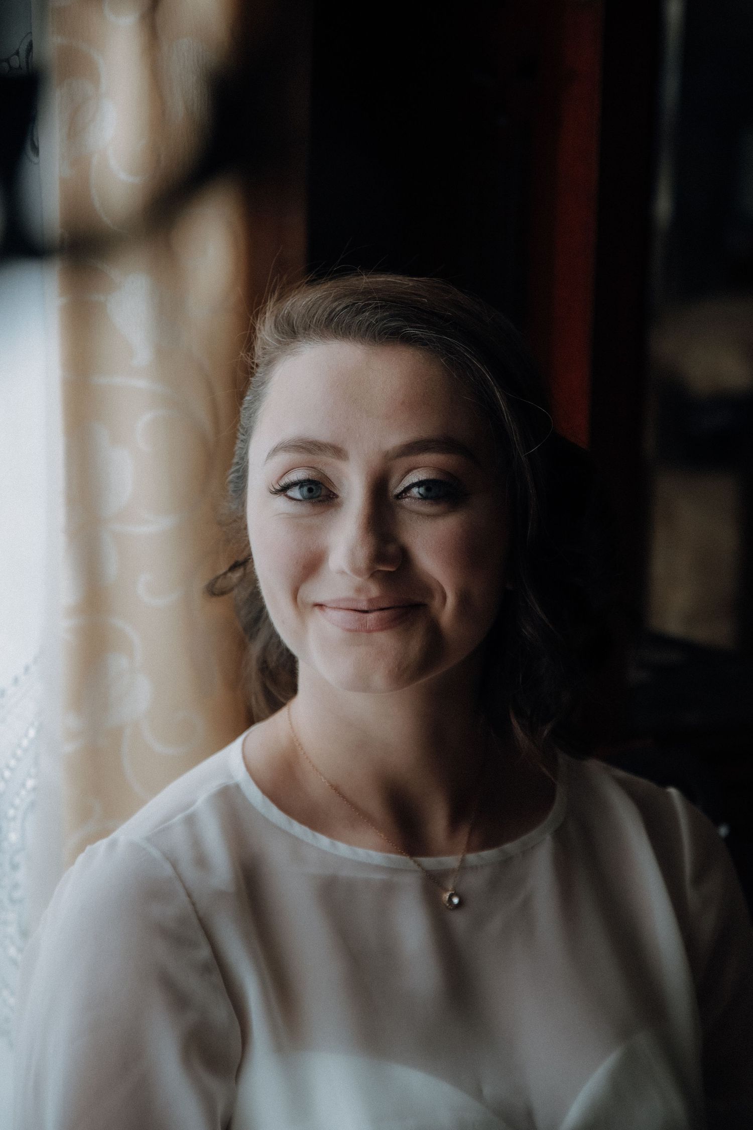 Portrait of bride in elegant white dress with natural light by window.