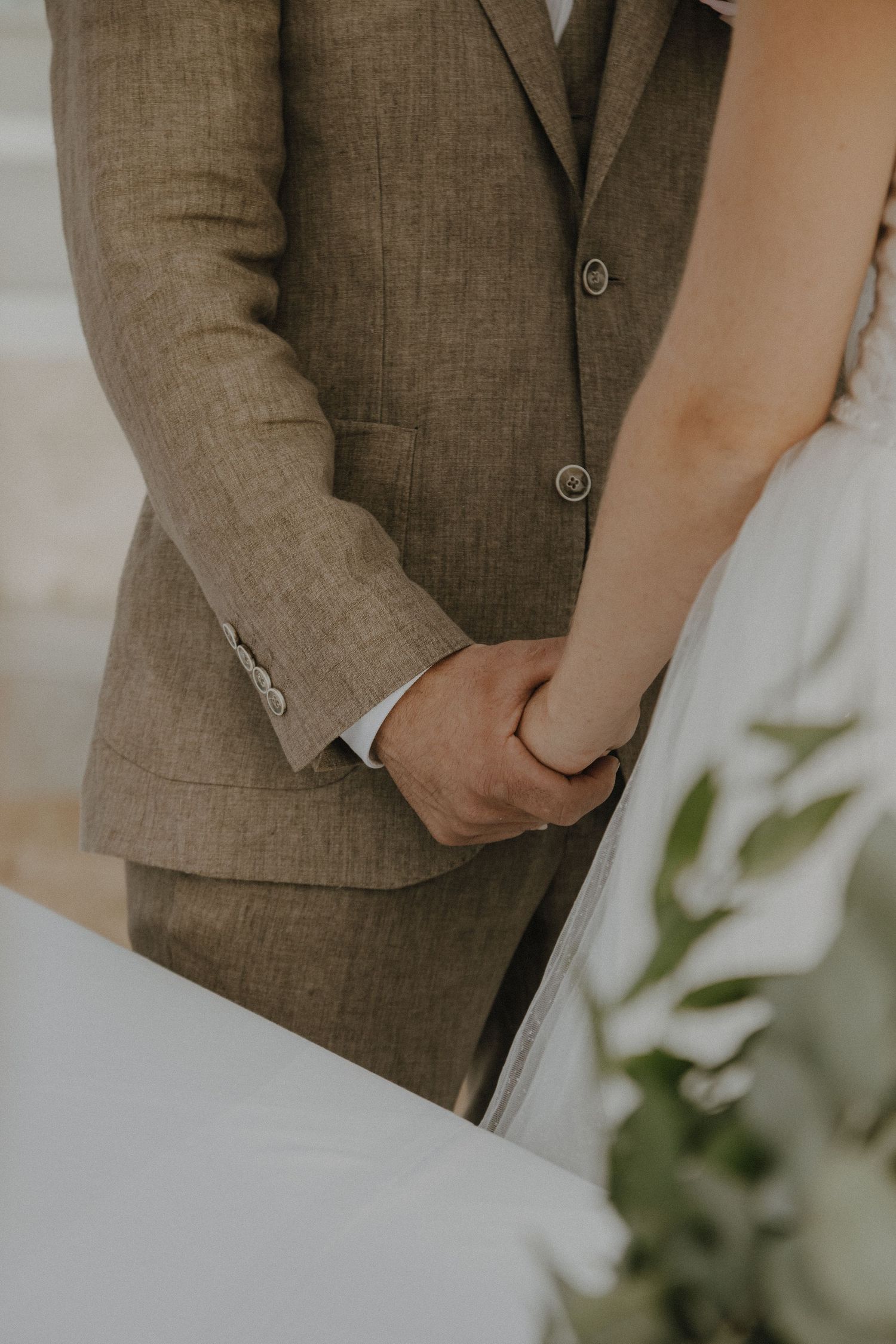 Close-up details of brown linen suit and white dress at beach wedding ceremony.