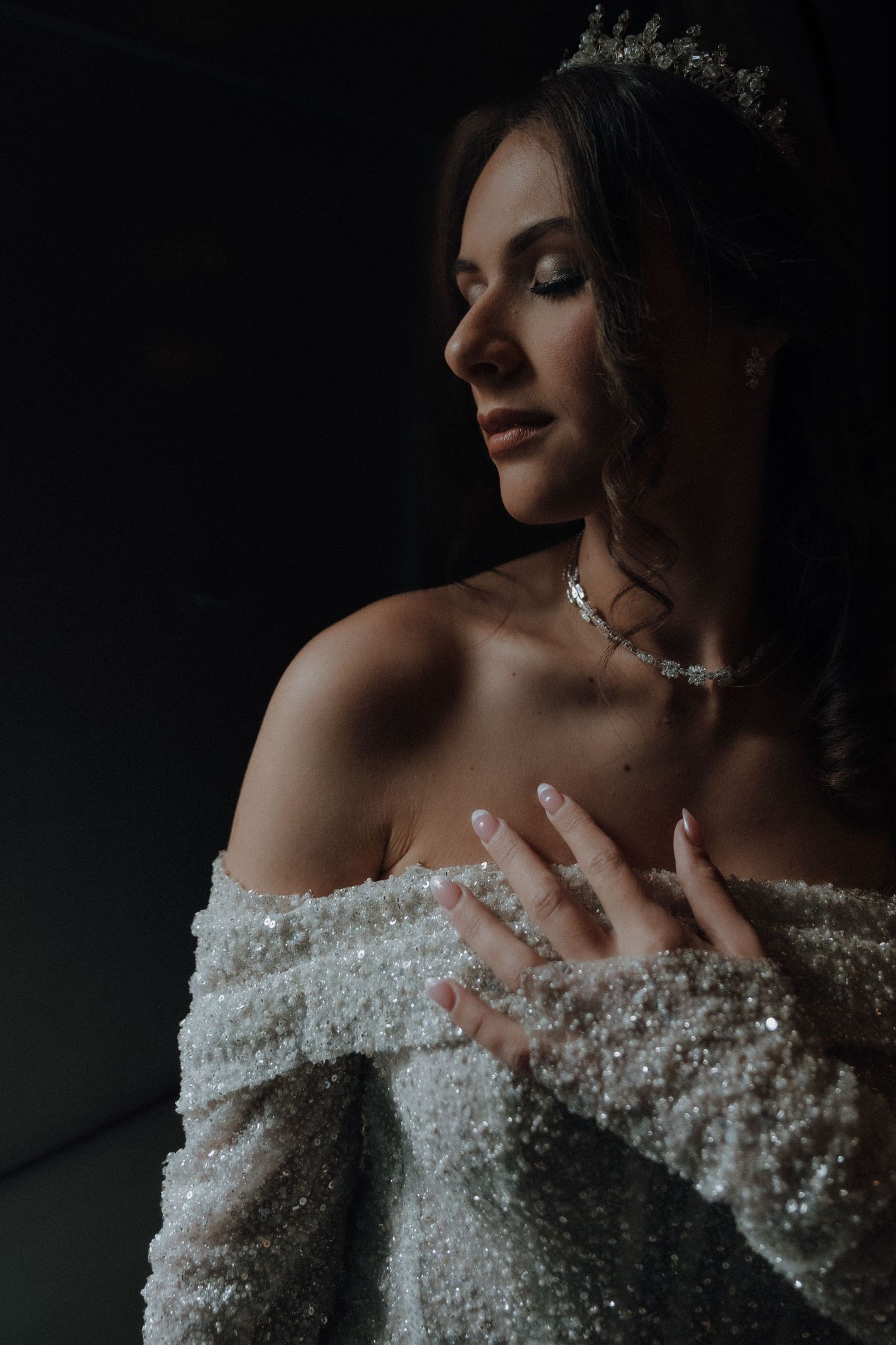 Dramatic side profile of bride wearing crystal crown and off-shoulder beaded gown.