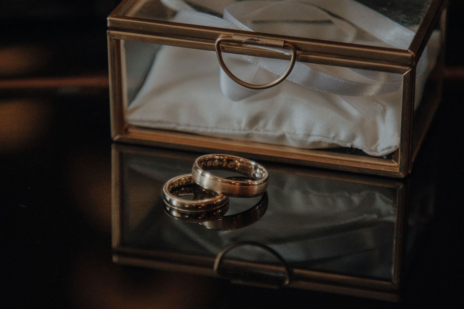 Wedding rings displayed elegantly in a glass box with mirror reflection.