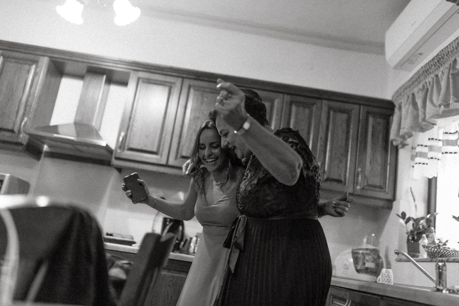 Black and white photo of people dancing and celebrating in a kitchen setting.