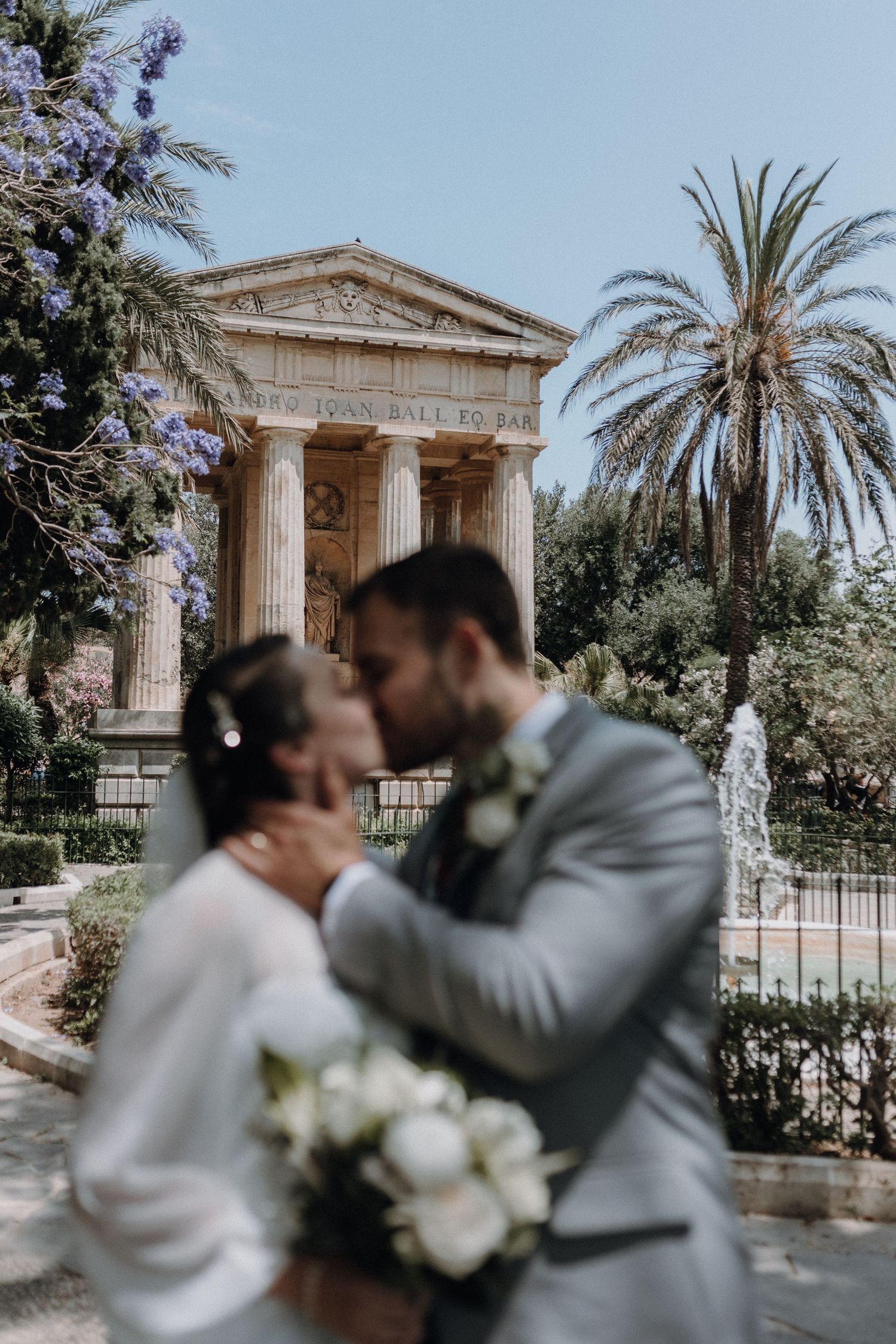 A romantic moment between newlyweds in front of a classical Mediterranean building.
