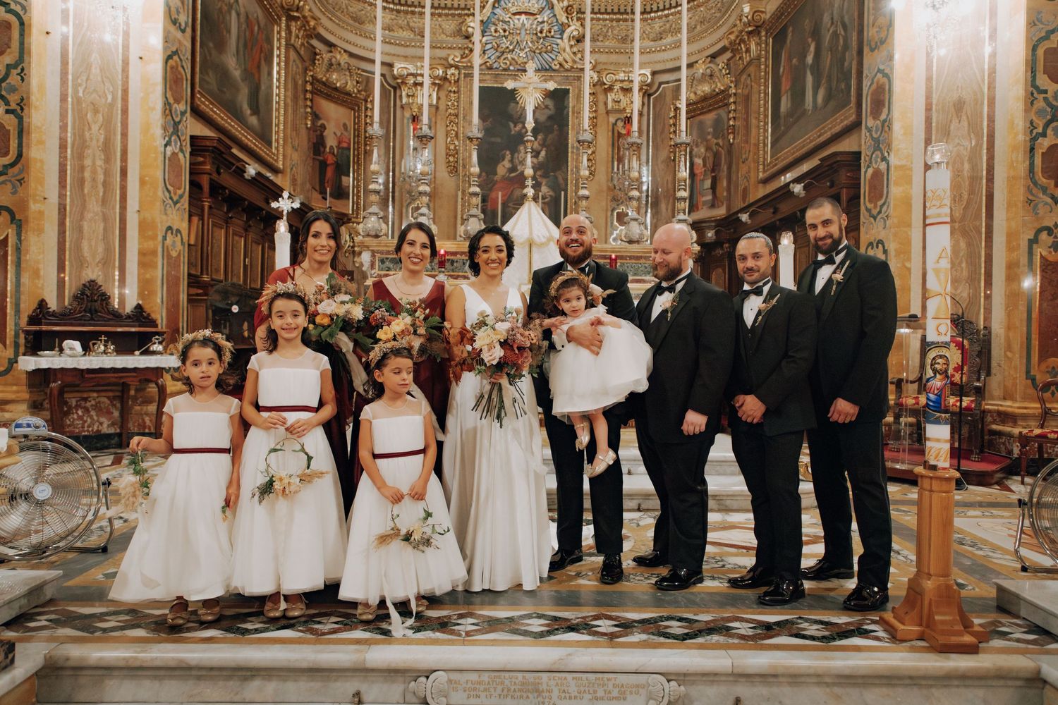 Wedding party members pose together inside historic church with elaborate altar and architectural details.