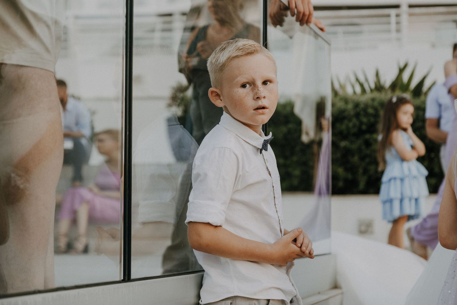 Young attendant in white dress shirt at formal event with reflective surfaces in background.