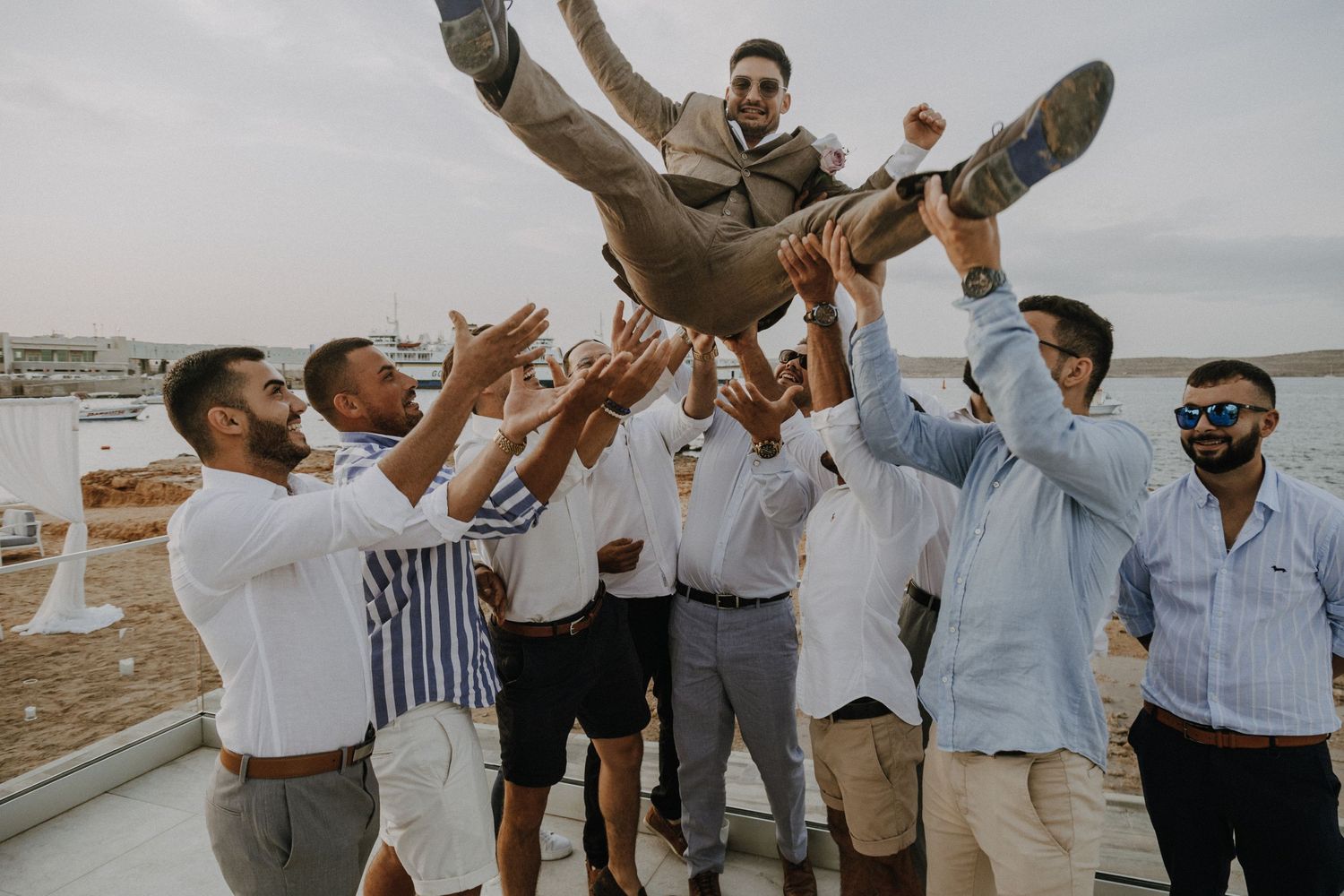 A group of friends jumping playfully outside with a cloudy sky in the background.