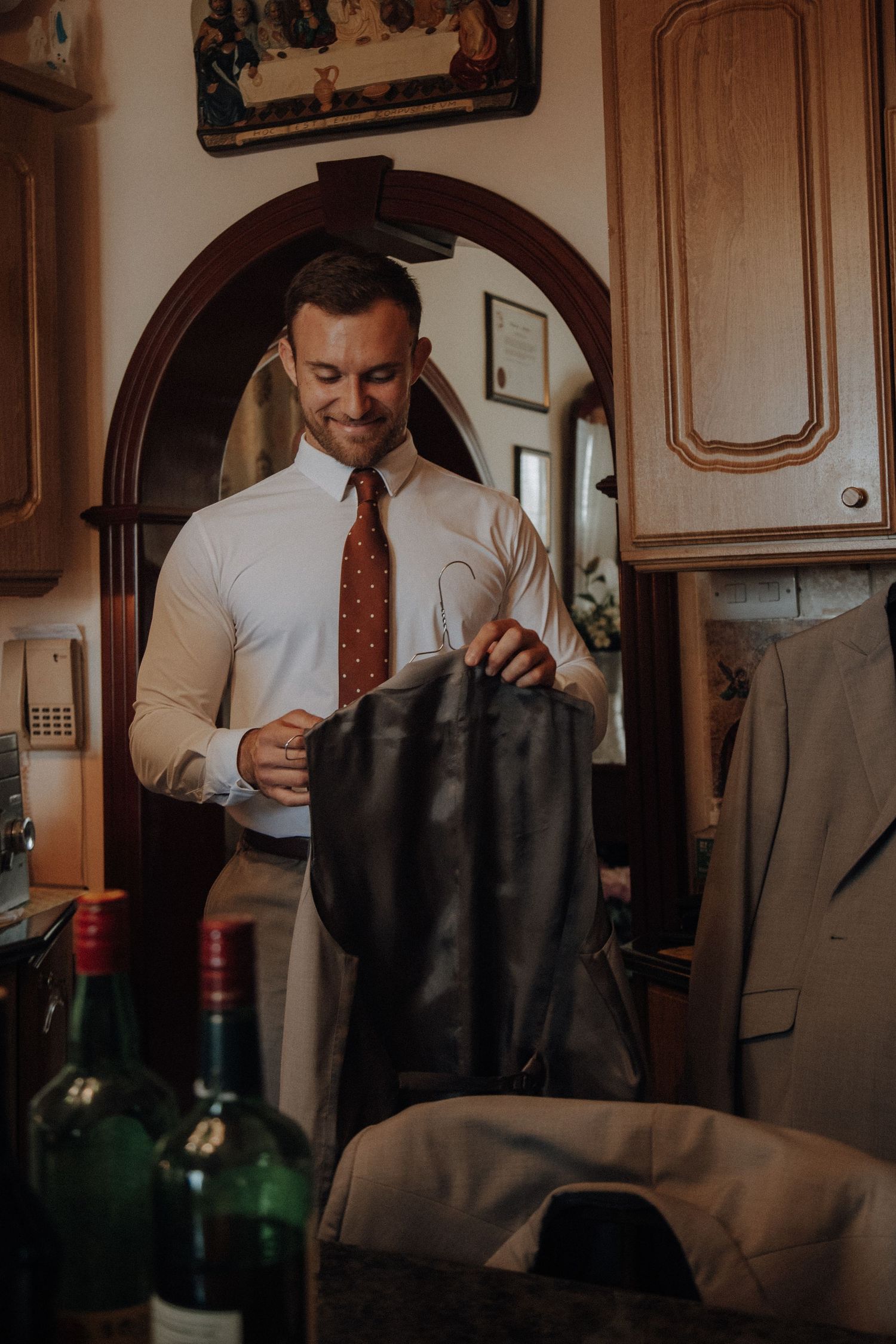 A person in white shirt and red tie handles formal attire in a traditional room setting.