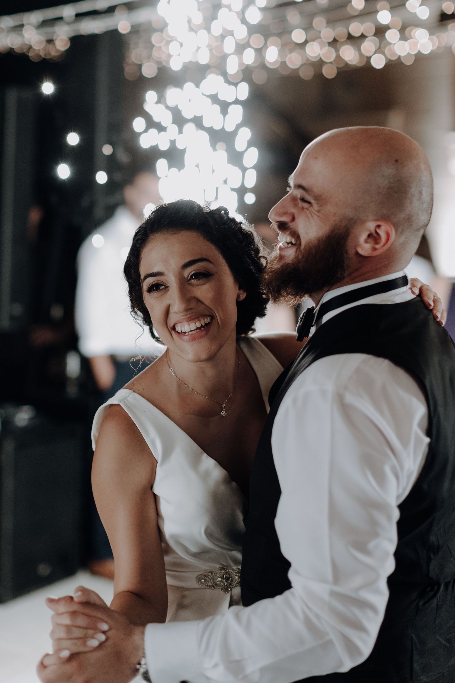 A couple shares a joyful moment on their wedding day under twinkling lights during their first dance.
