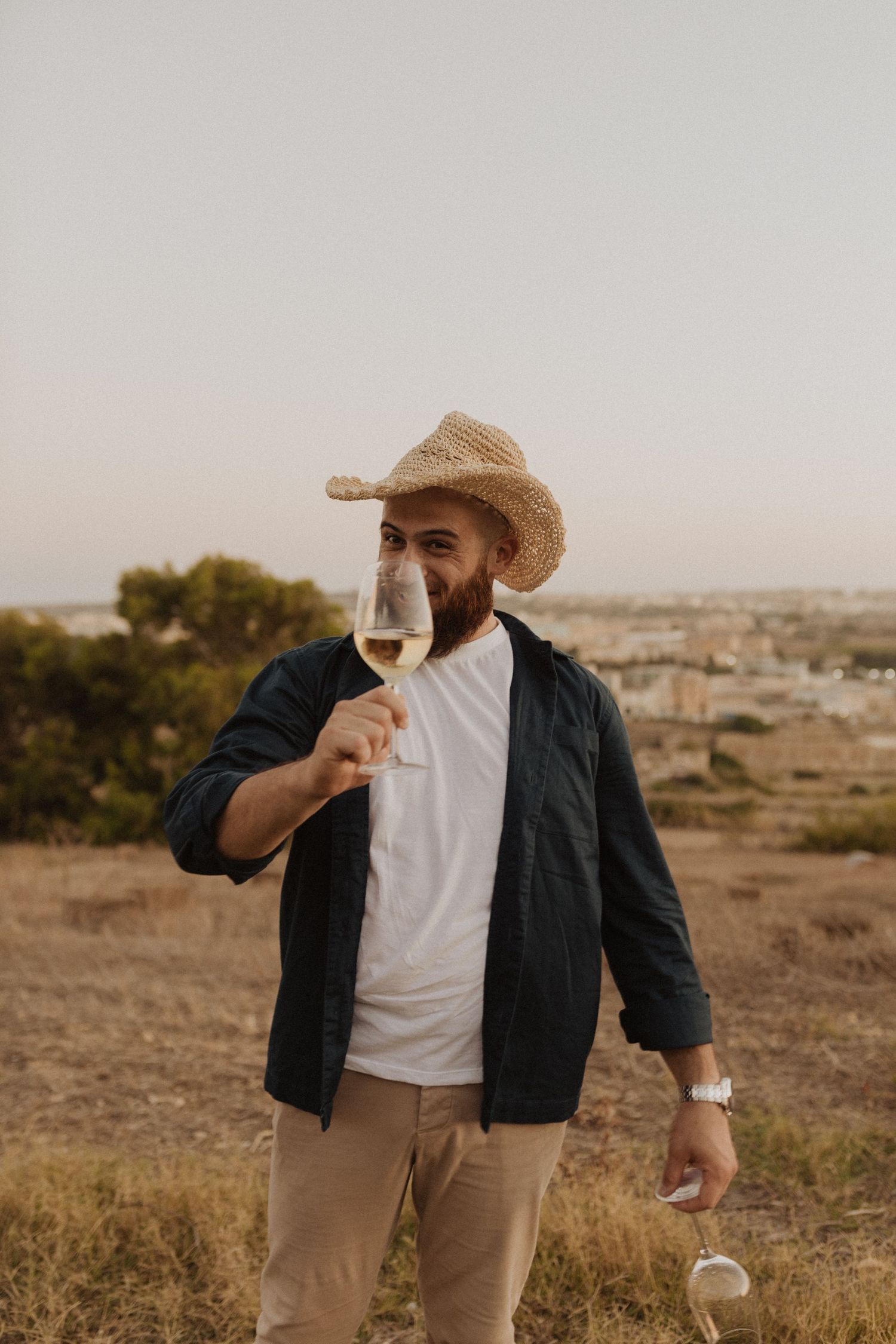 Person in casual attire holding wine glass against desert landscape at golden hour.