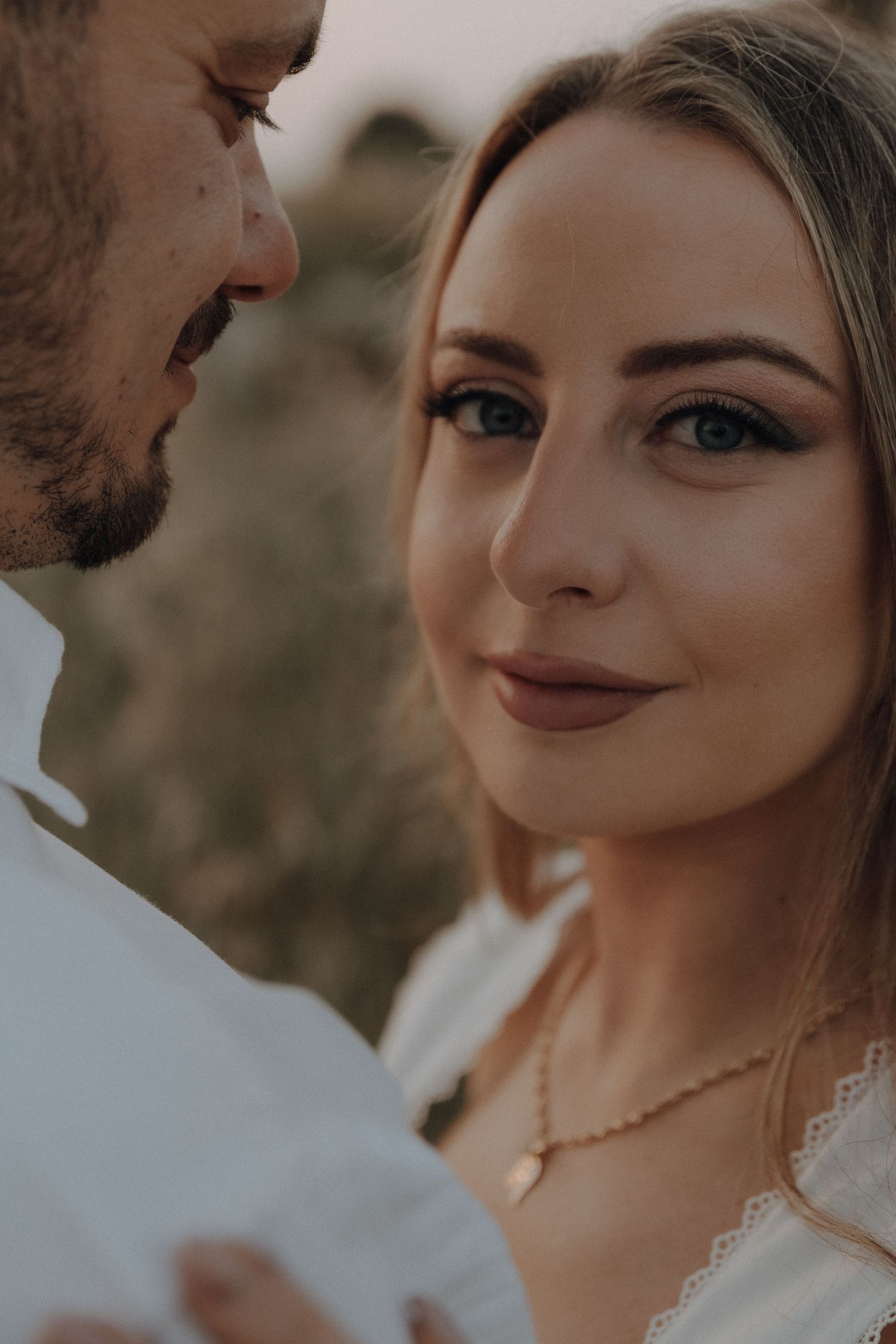 Close-up portrait of a blonde woman in a white lace dress looking at her partner during a golden hour photo shoot.