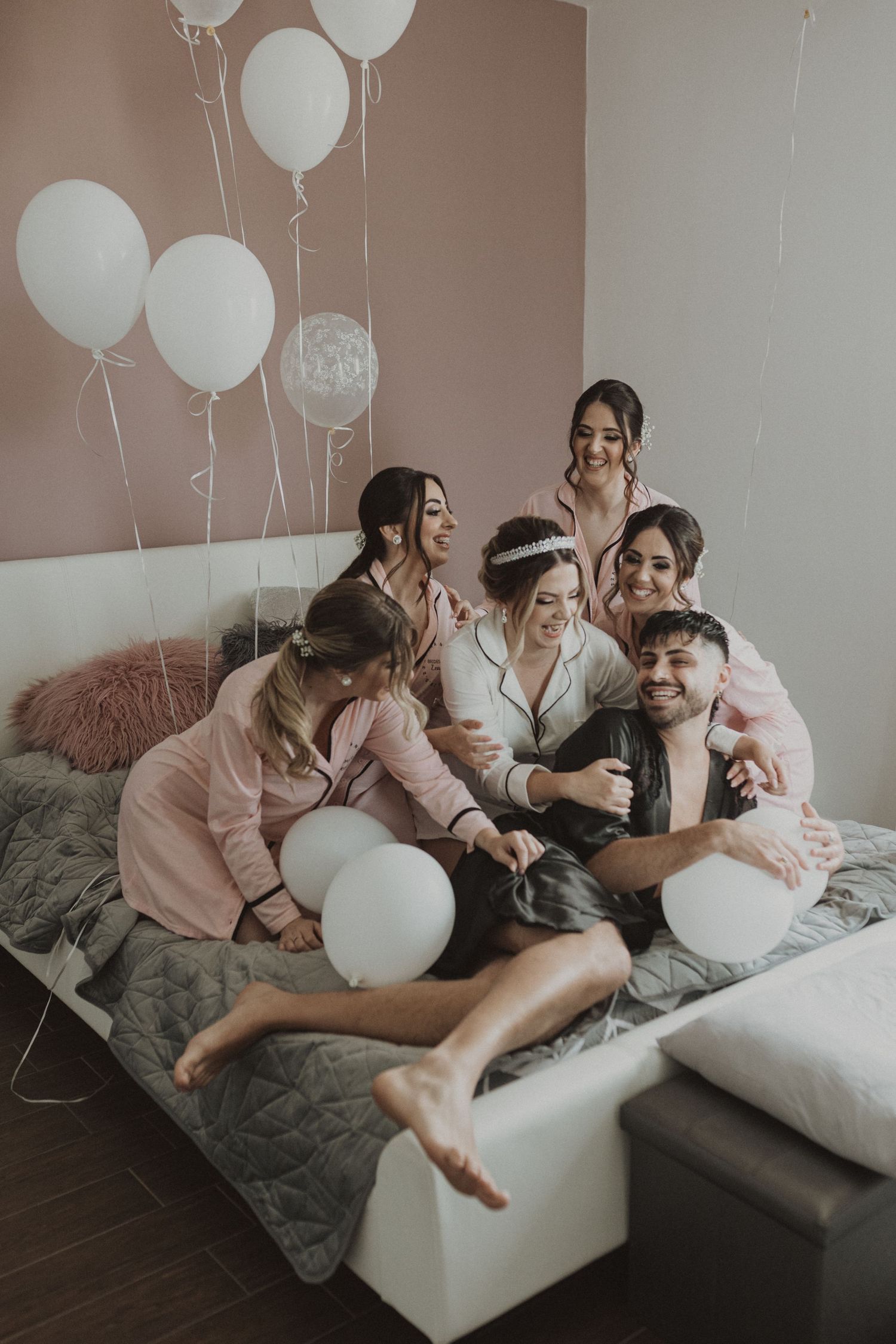 Intimate pre-wedding moment with bridesmaids and bride laughing together on bed with balloons.