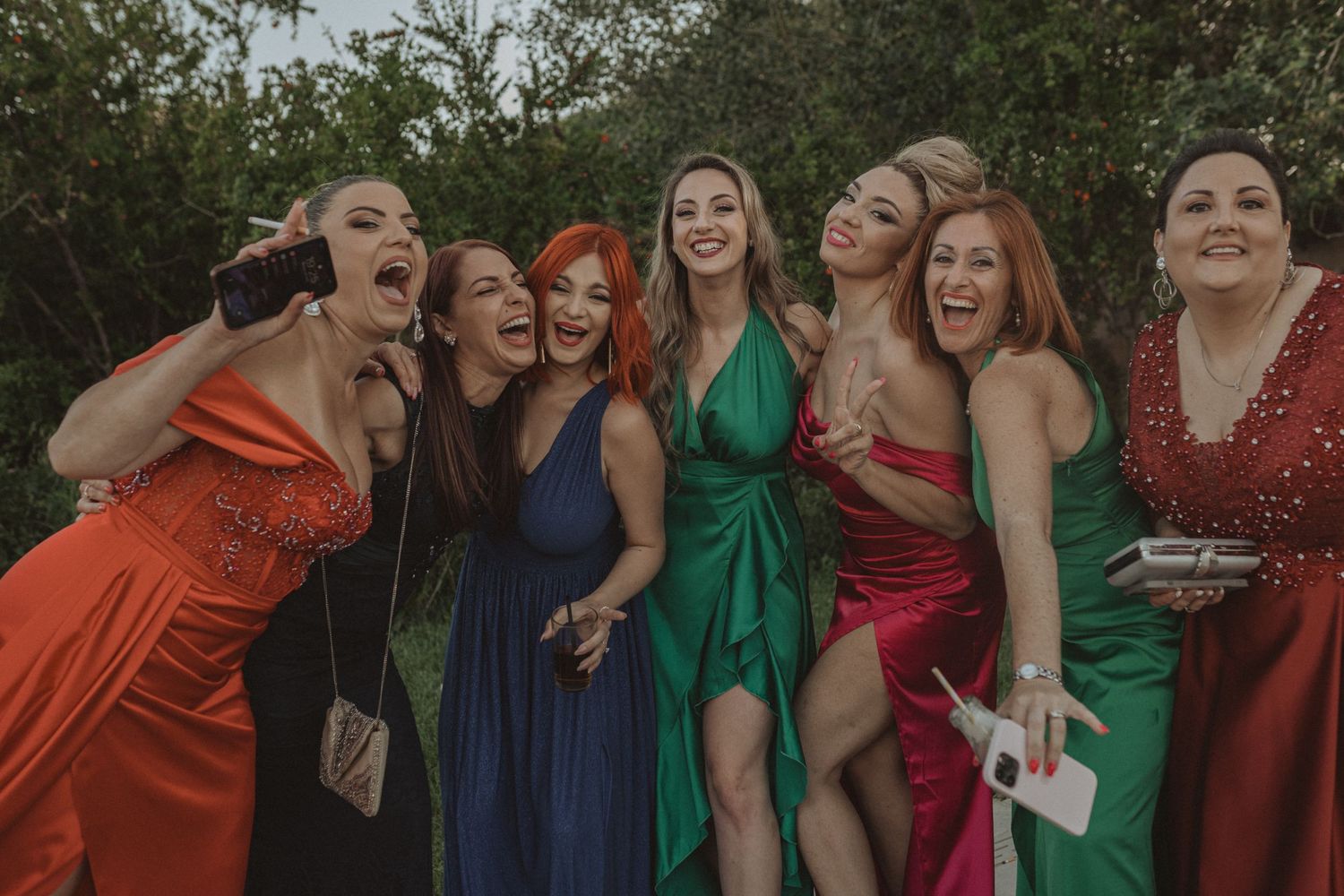 Bridesmaids in jewel-toned dresses laugh and celebrate during outdoor photo session.