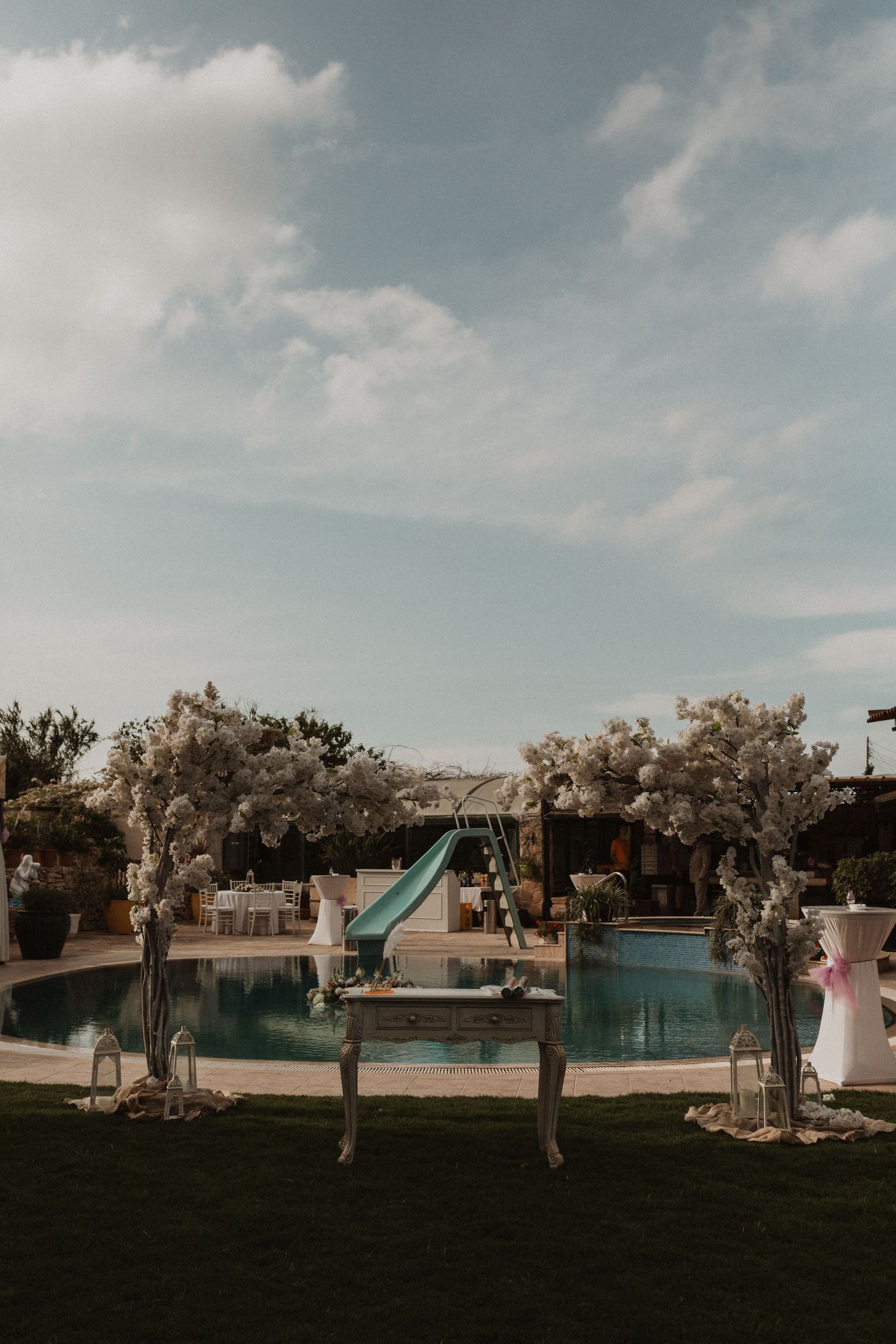 Lakeside wedding venue setup with tall vases and floral arrangements against blue sky.