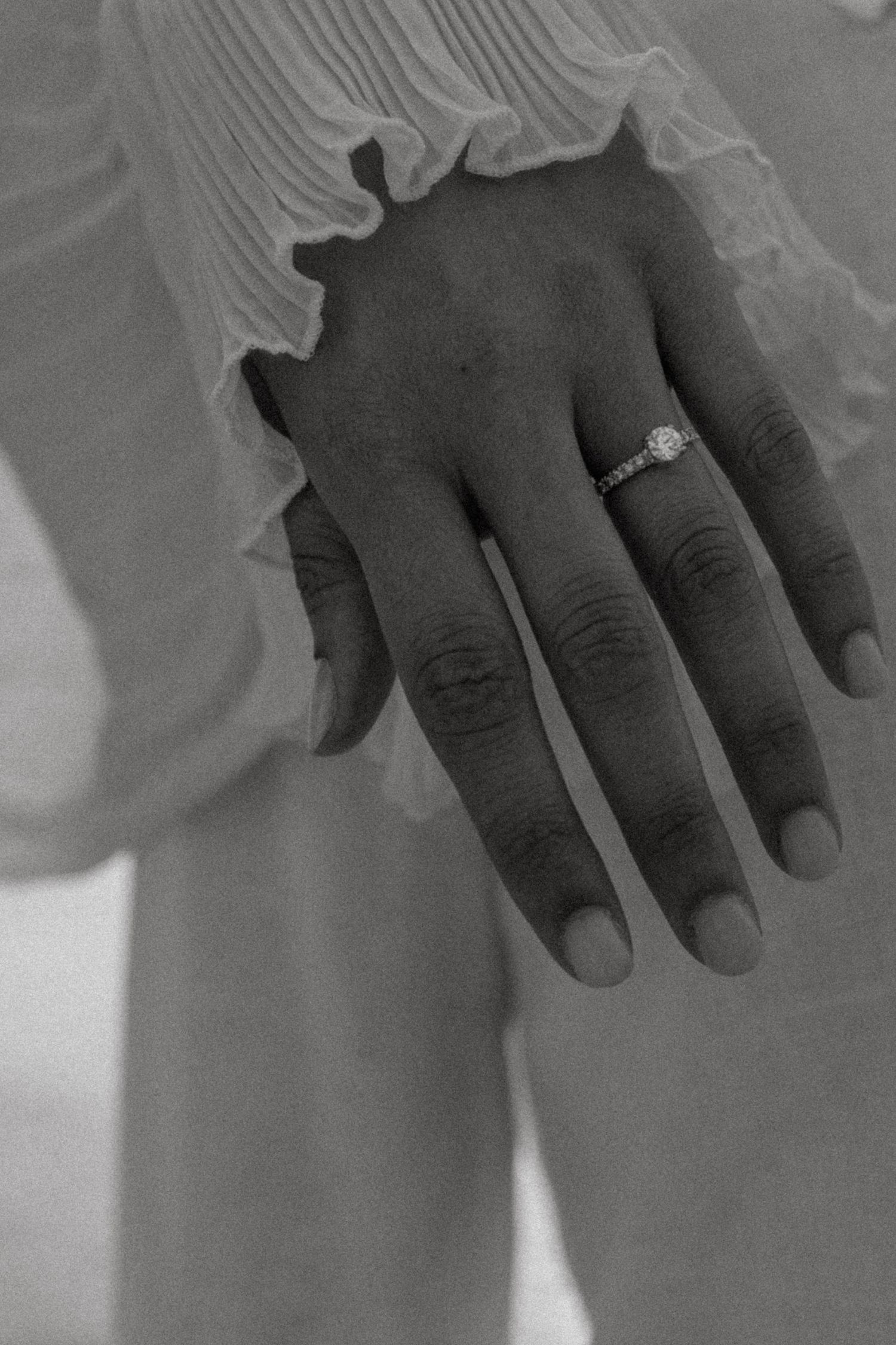 A close-up black and white photo of an engagement ring on a hand.