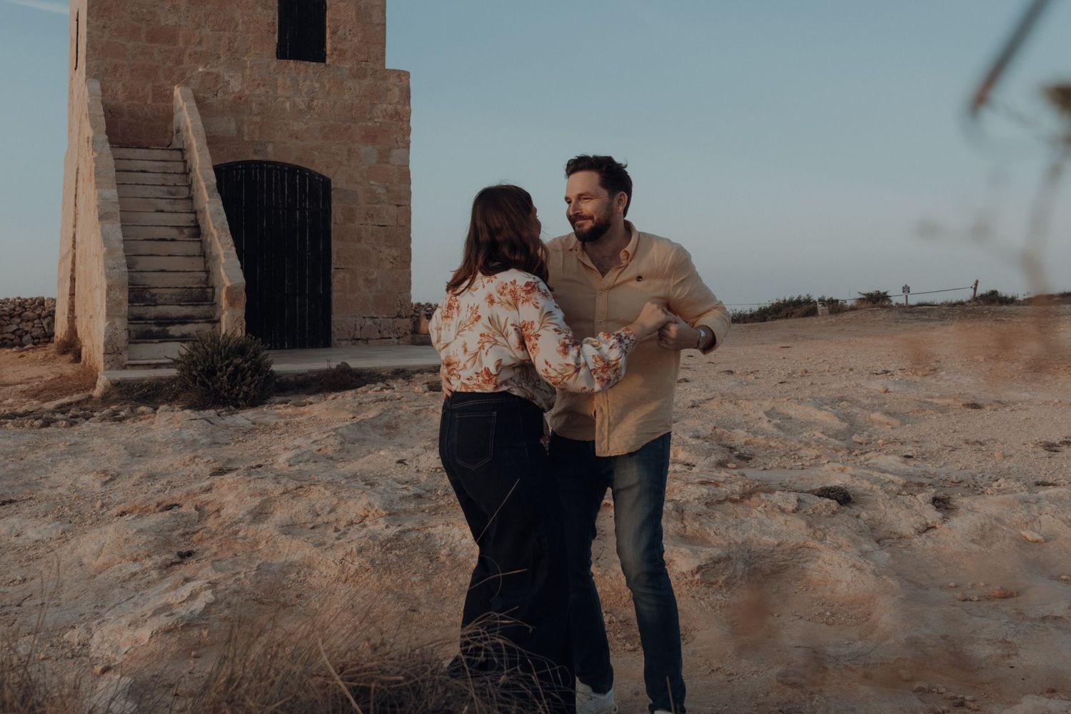 A couple walks together along a sandy beach at sunset holding hands and enjoying a romantic moment.