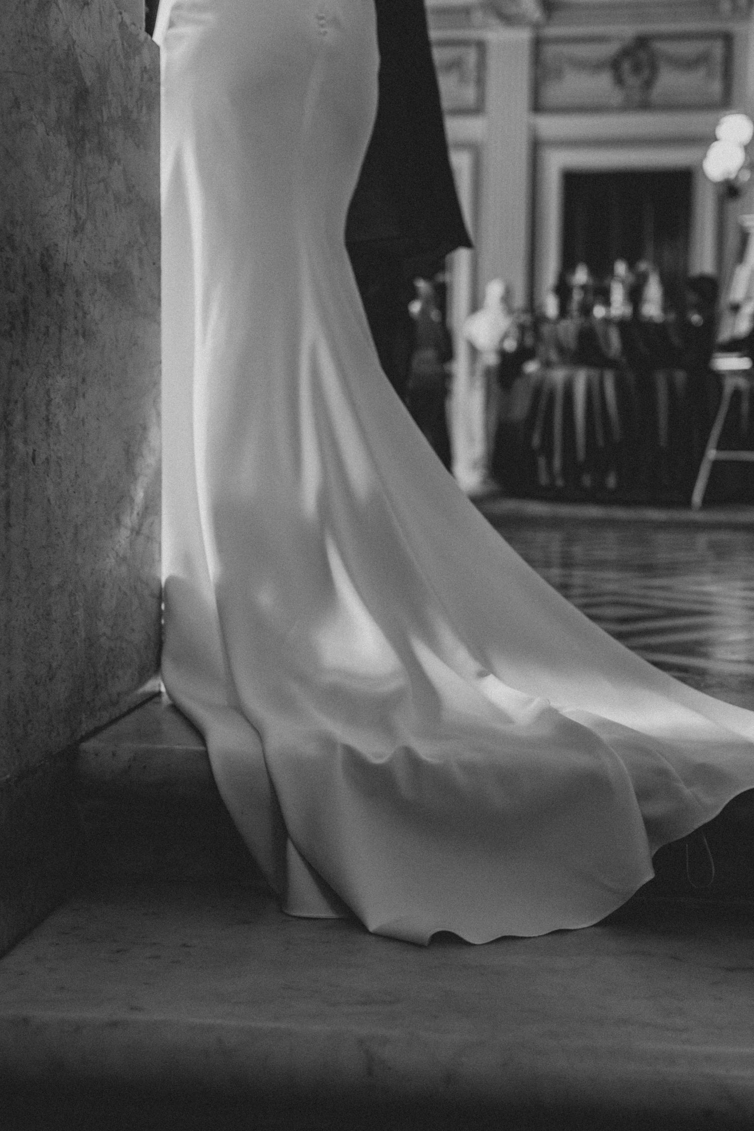 Close-up of flowing white wedding dress train against dark hardwood floor in elegant venue.