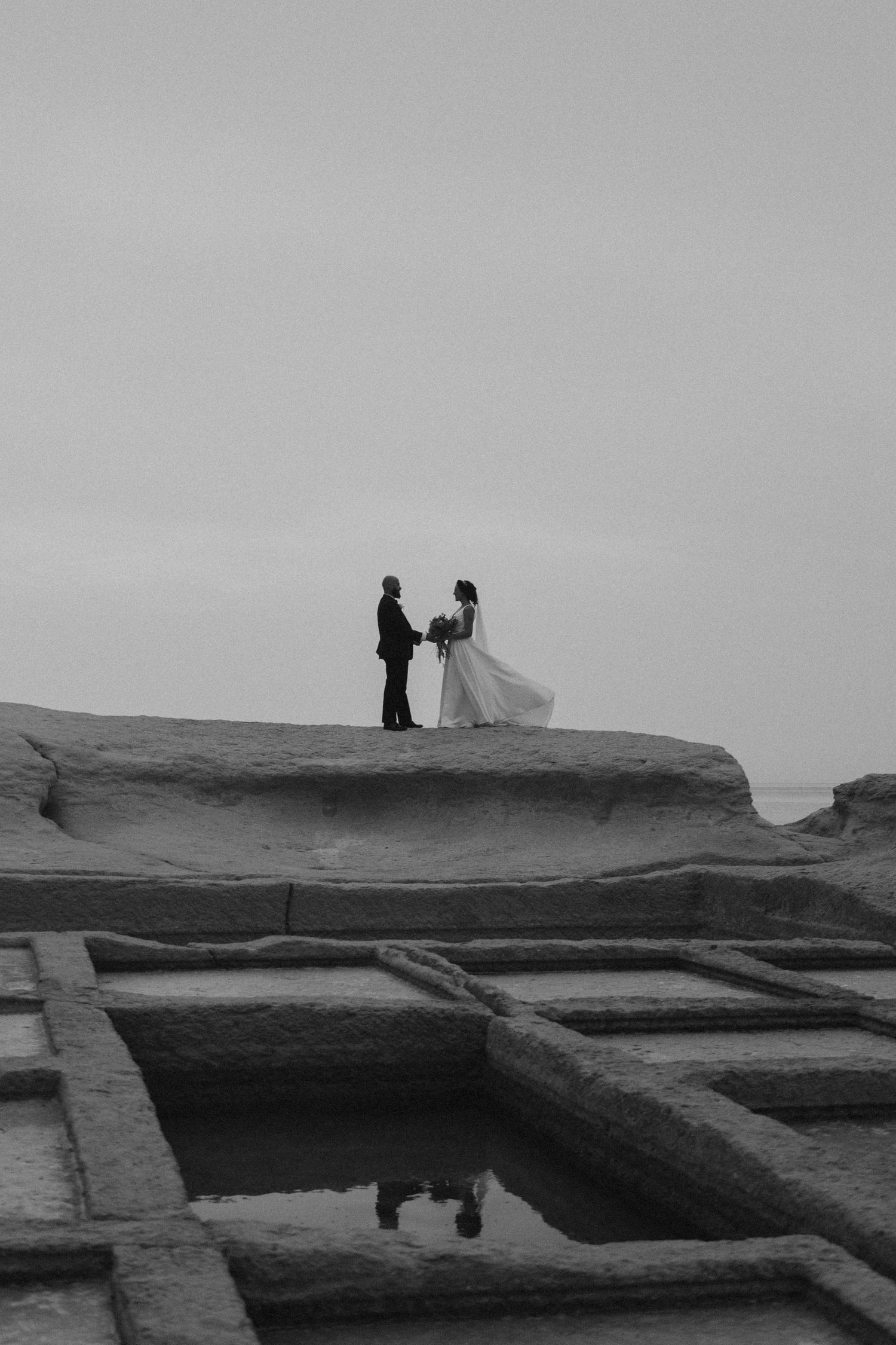A dramatic black and white silhouette of a couple on their wedding day atop coastal rock formations.