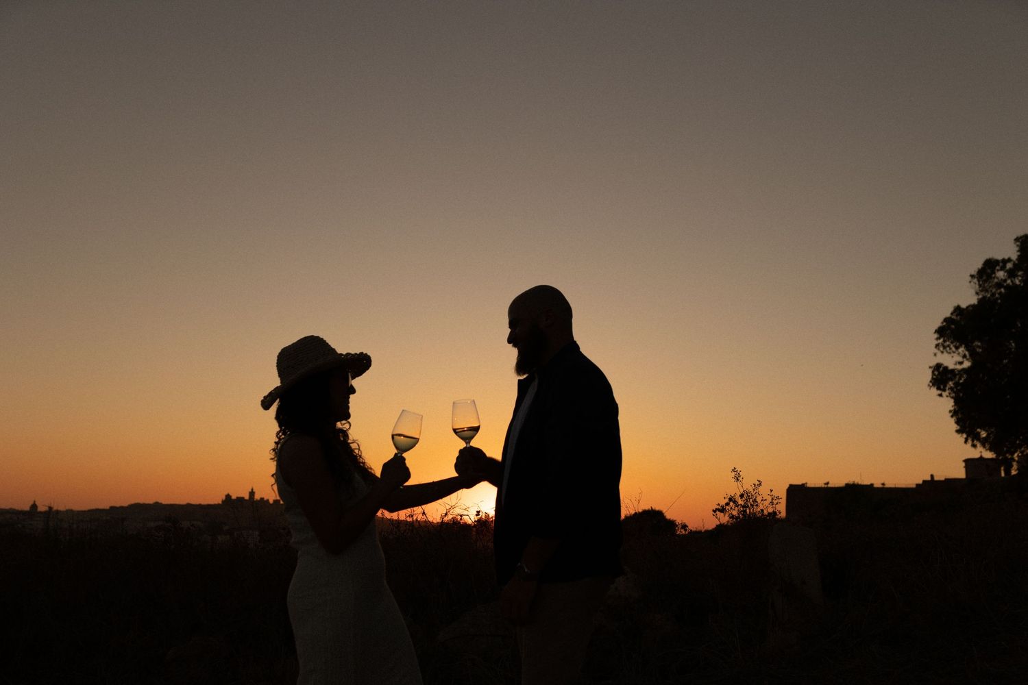 Silhouettes of a couple enjoying drinks against a dramatic sunset sky.
