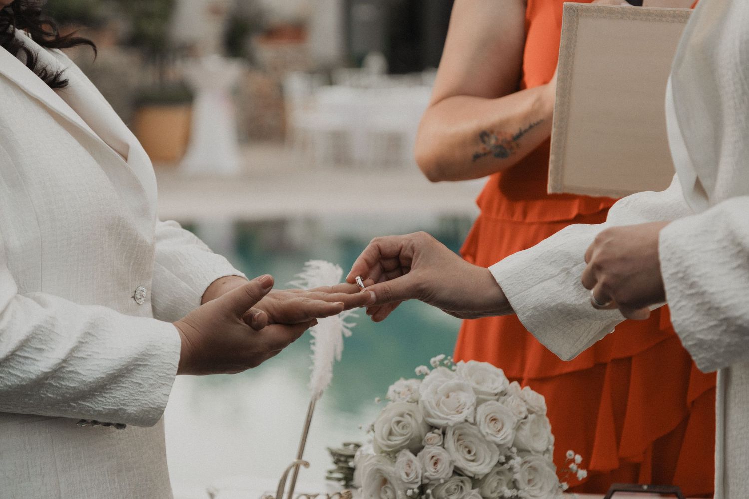 Intimate moment of ring exchange during wedding ceremony with white roses in foreground.