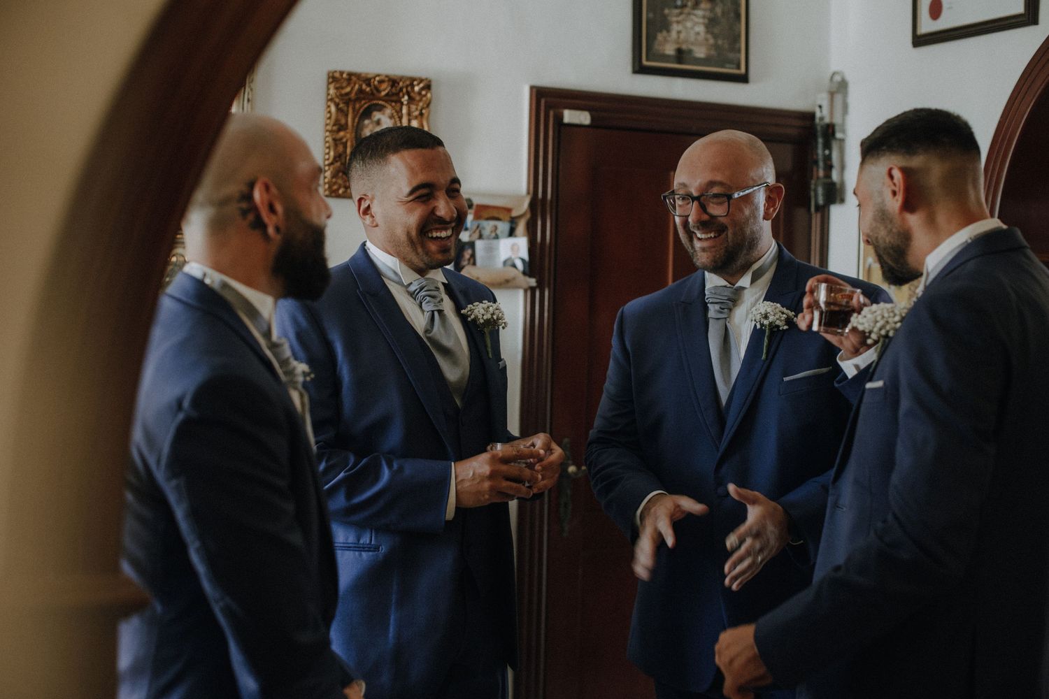 Wedding party members in blue suits engage in conversation before the ceremony.