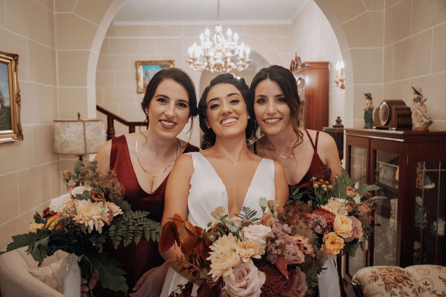 A bridal party poses with bouquets of pink and cream flowers in an elegant room.