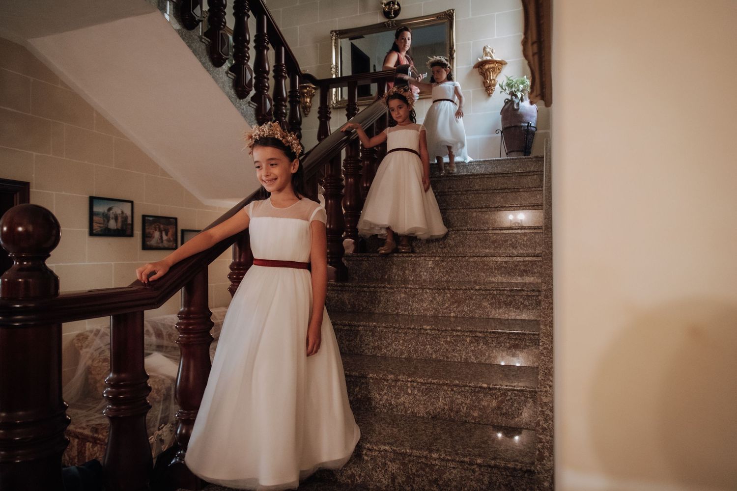 A young attendant in a white dress descends an elegant staircase during a formal event.