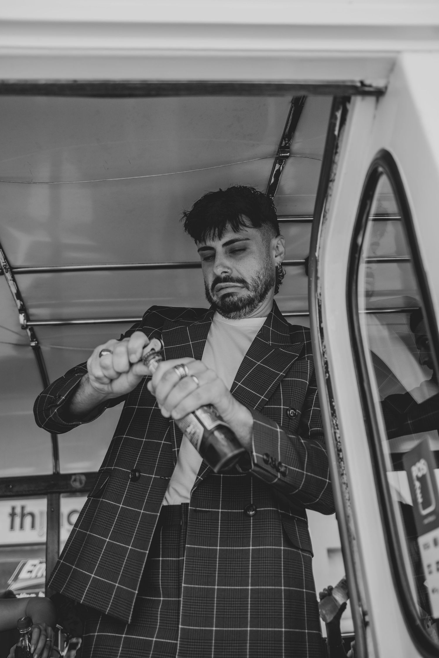 Man in checkered suit opens champagne bottle inside vintage bus.