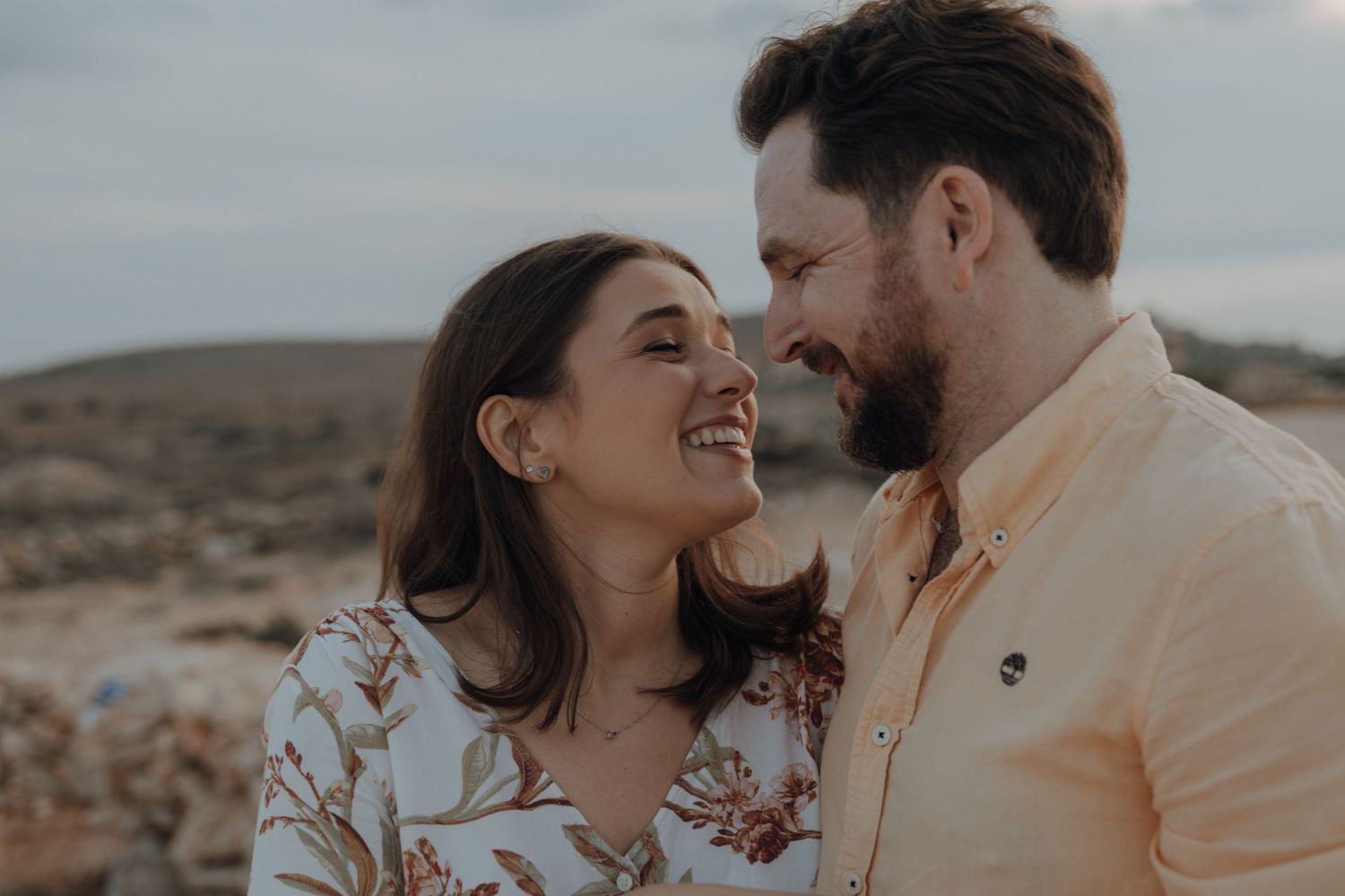 Couple sharing intimate moments in a desert setting while wearing coordinated light-colored outfits.