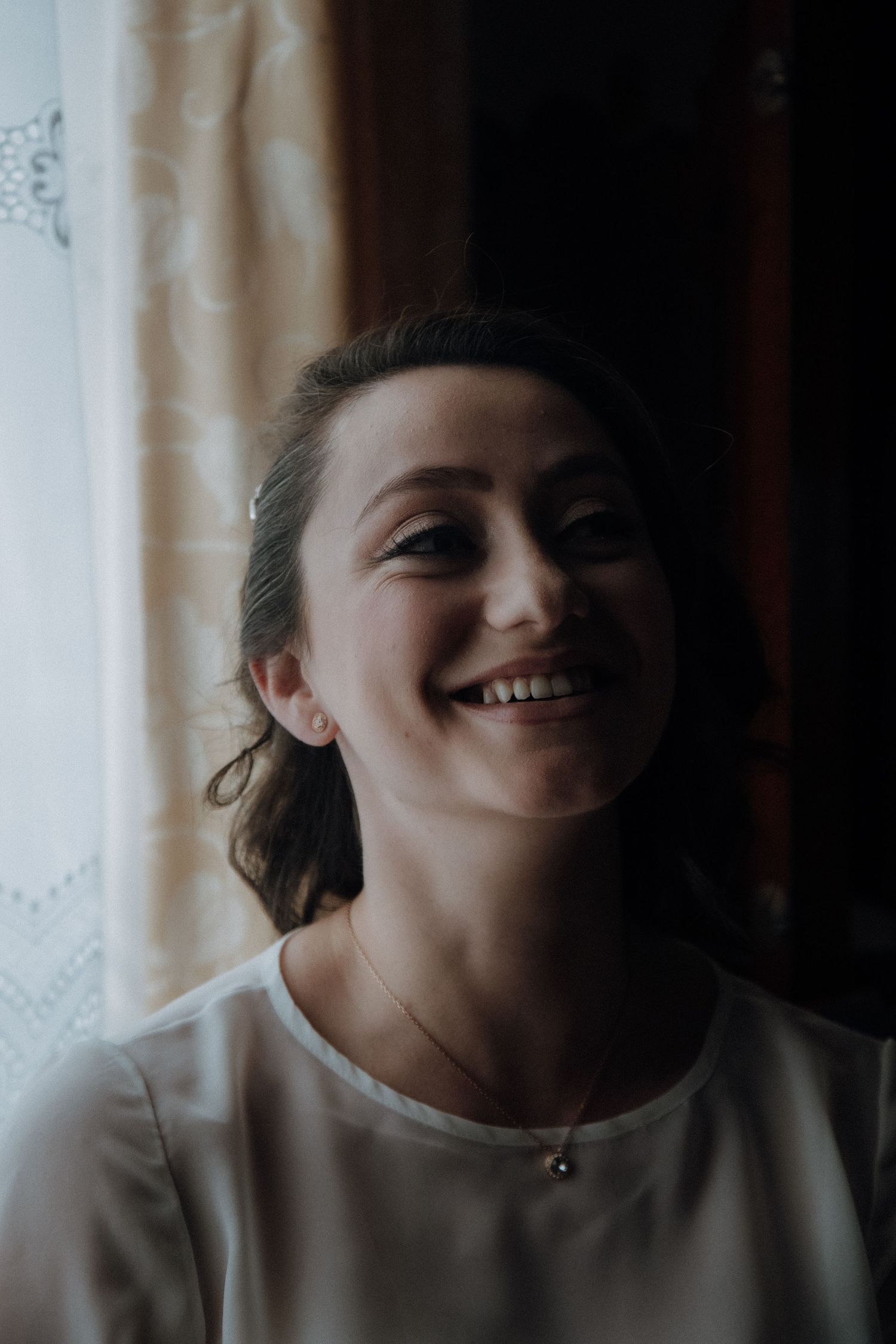 Natural light portrait of bride smiling warmly in white dress.