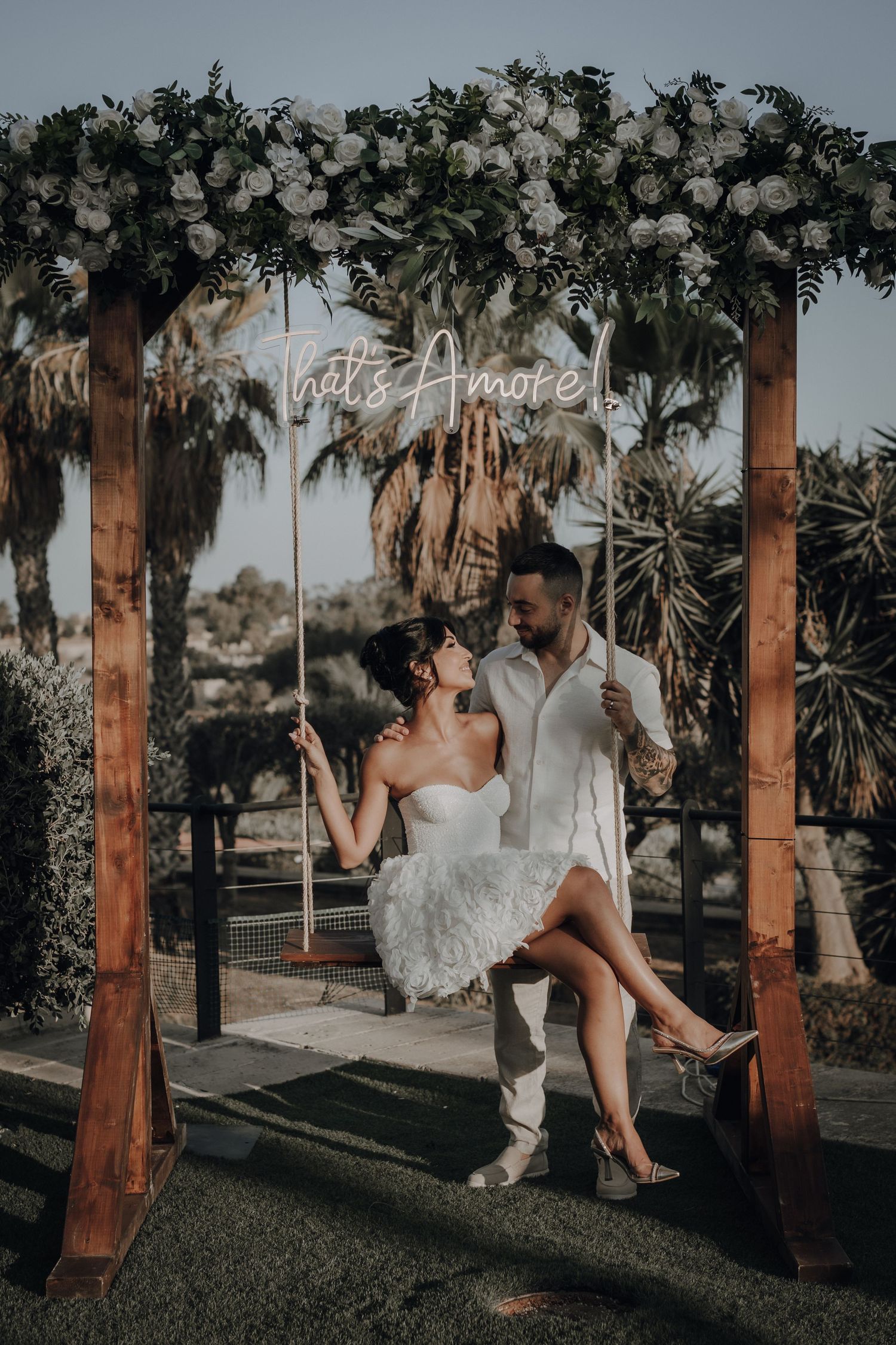 Romantic wedding photos under a floral arch with palm trees in the background.