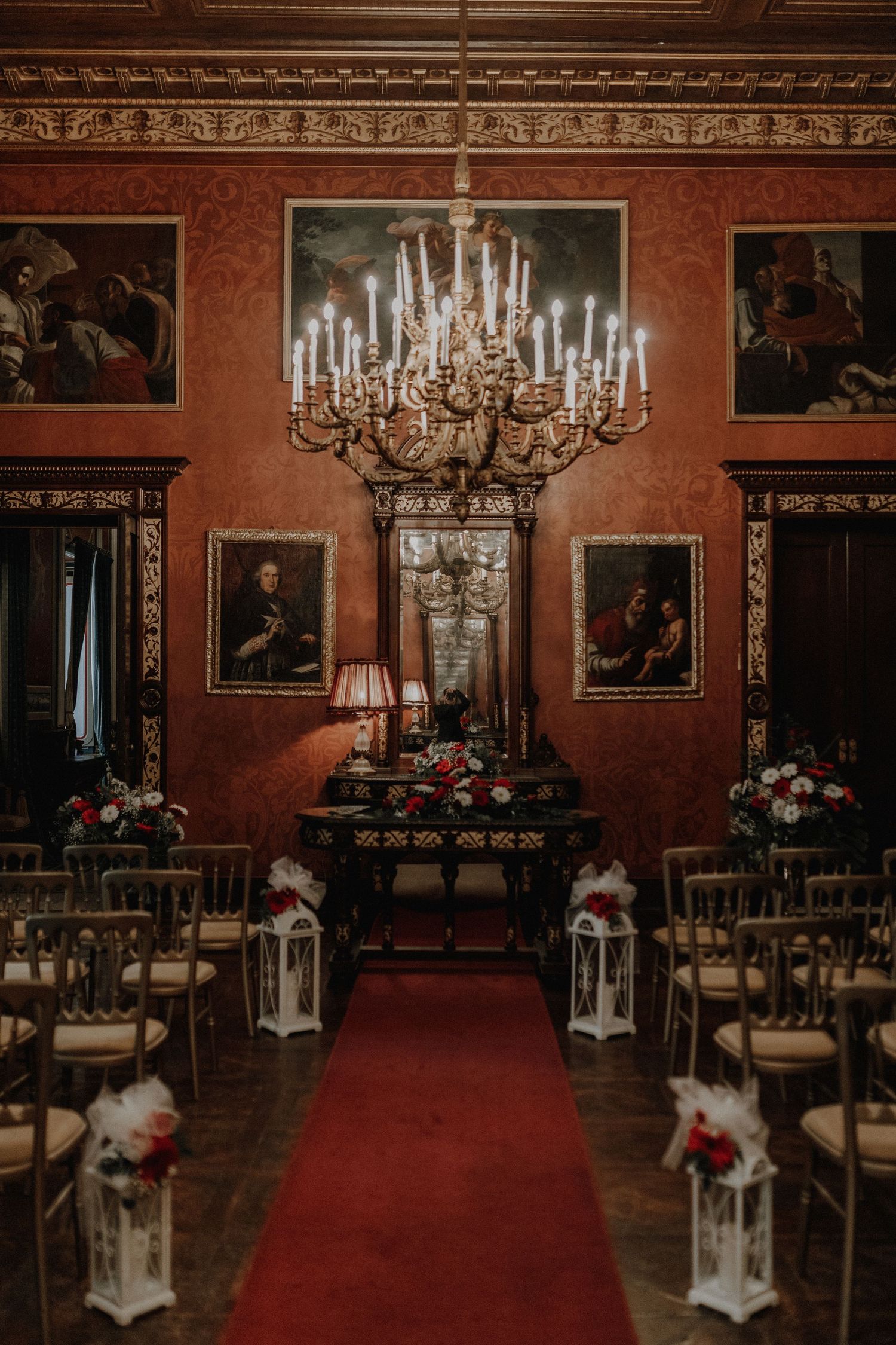 Historic palace interior with grand chandelier, red carpet aisle, and lantern decorations.