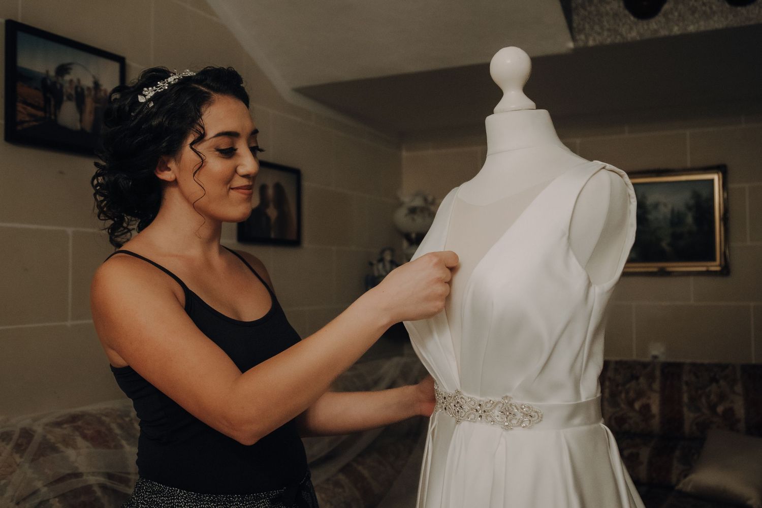 Woman adjusts white wedding dress on mannequin form in preparation for ceremony.