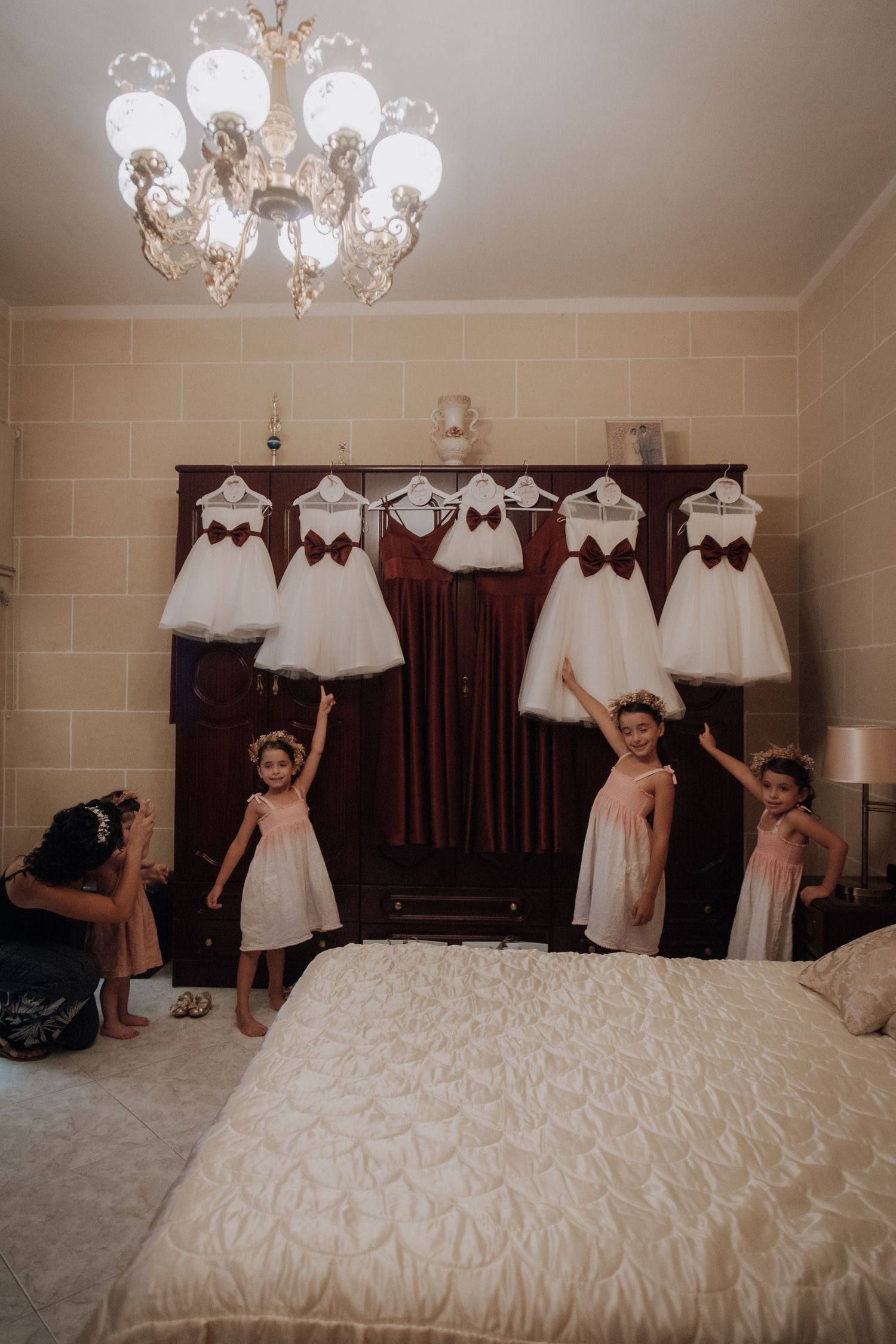 Room with multiple white dresses hanging and children playing on a bed below.