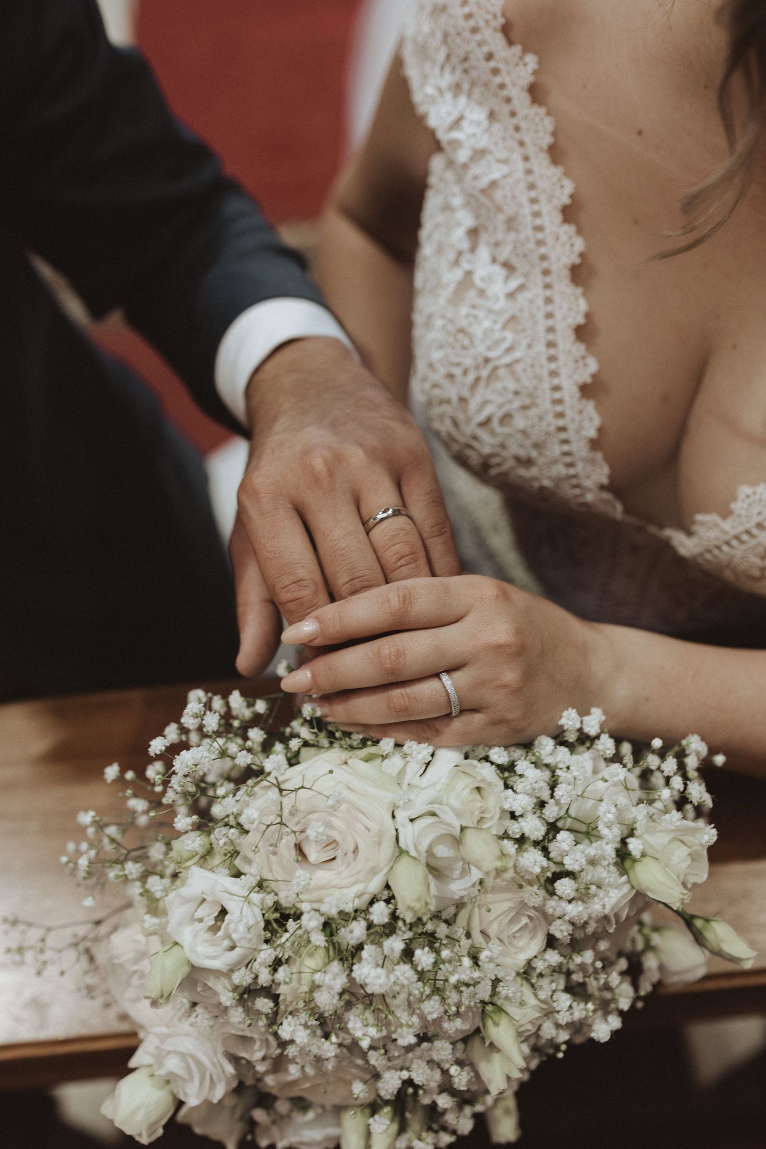 Wedding rings and hands resting on delicate white rose and baby's breath bouquet.
