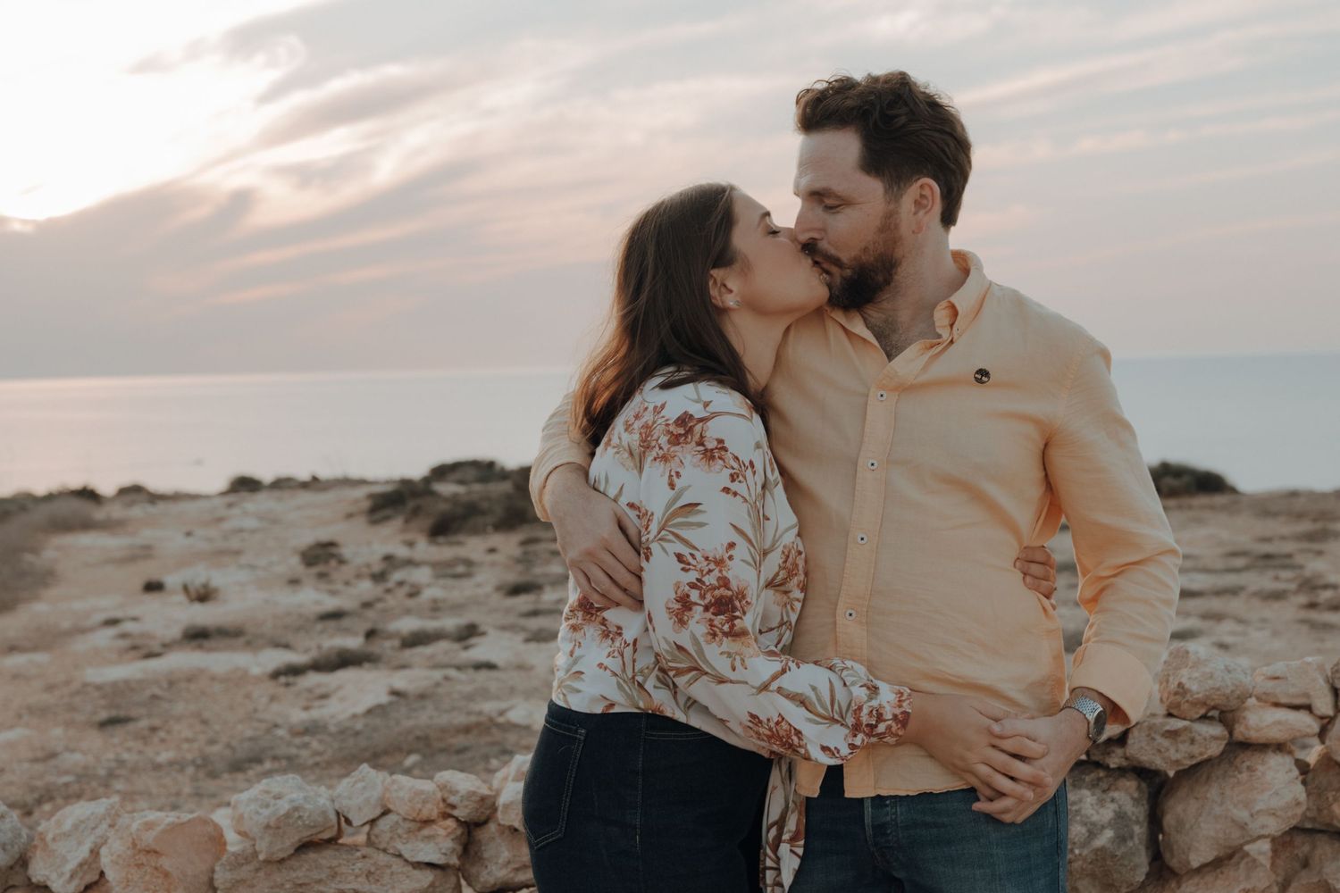 Couple laughing and embracing during sunset photoshoot in desert terrain with rocky landscape.