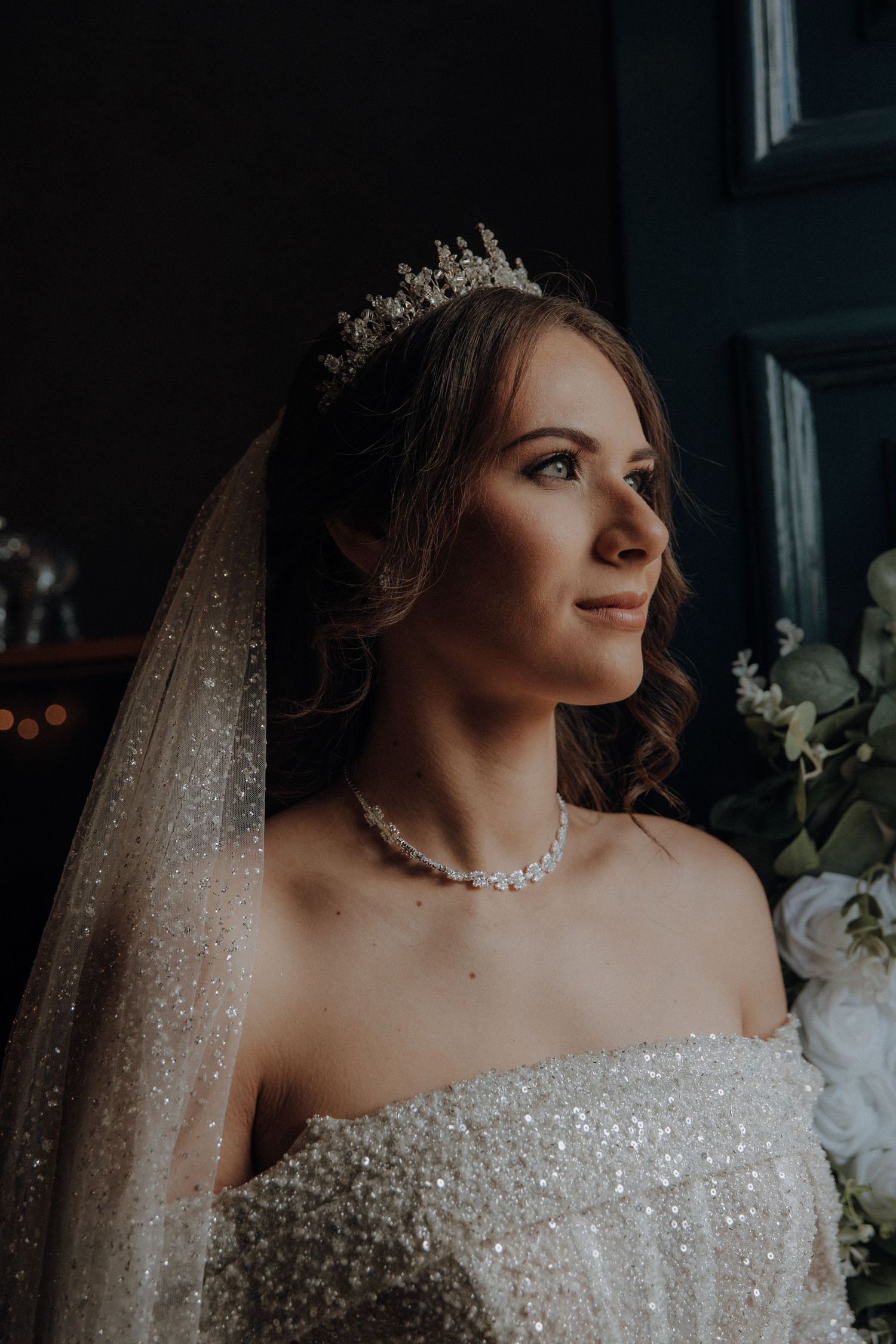 Bride in tiara and sparkly dress looking away in dramatic portrait.